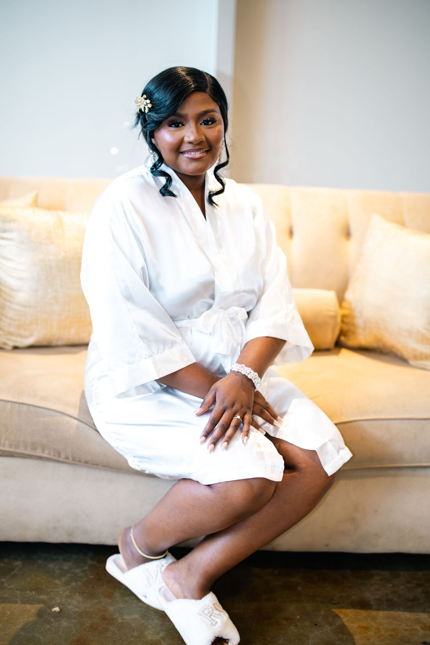 A person in a white robe sits casually on a cream colored couch in a bright room.