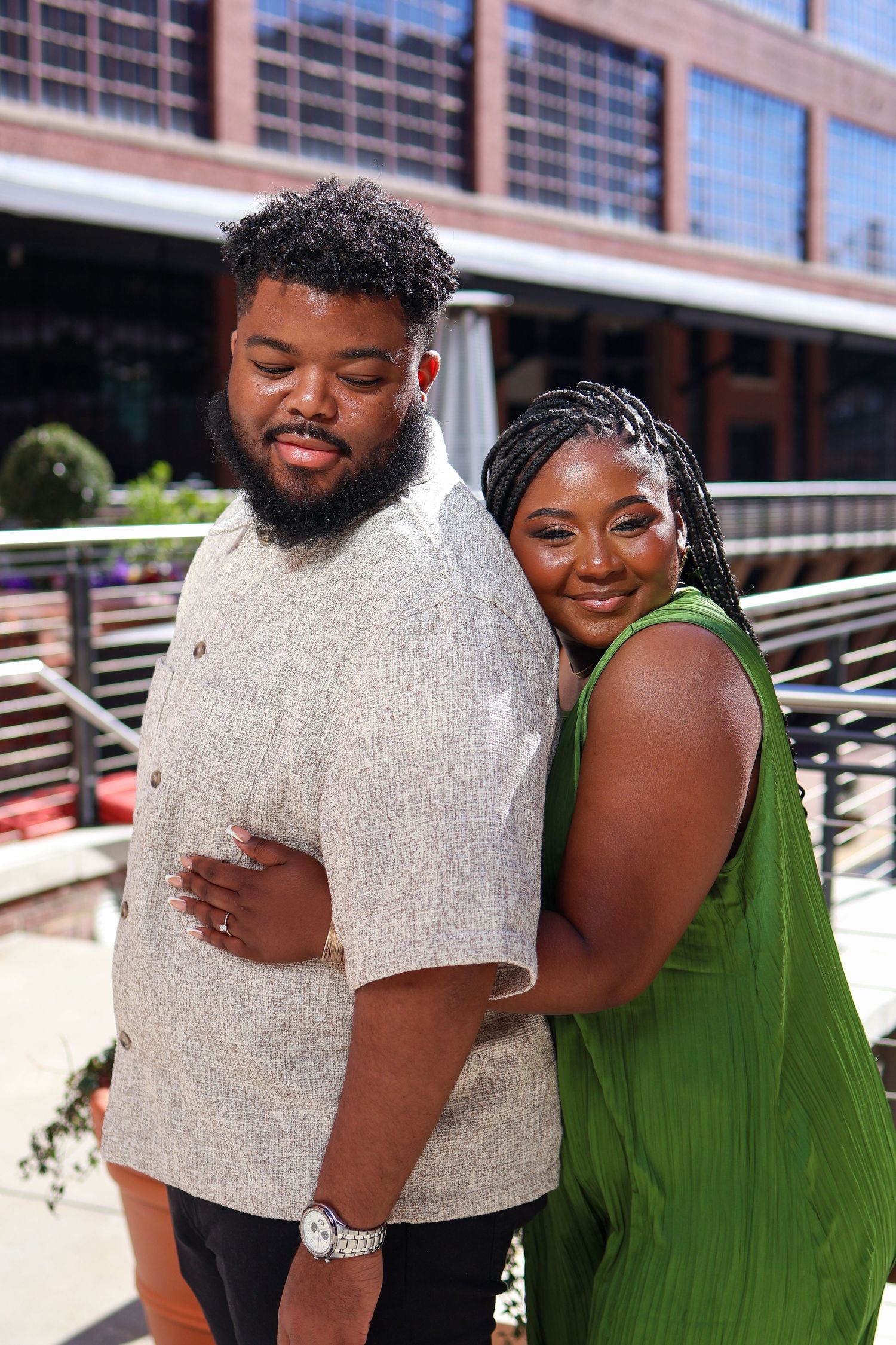 A happy couple embraces outdoors in front of an industrial brick building.