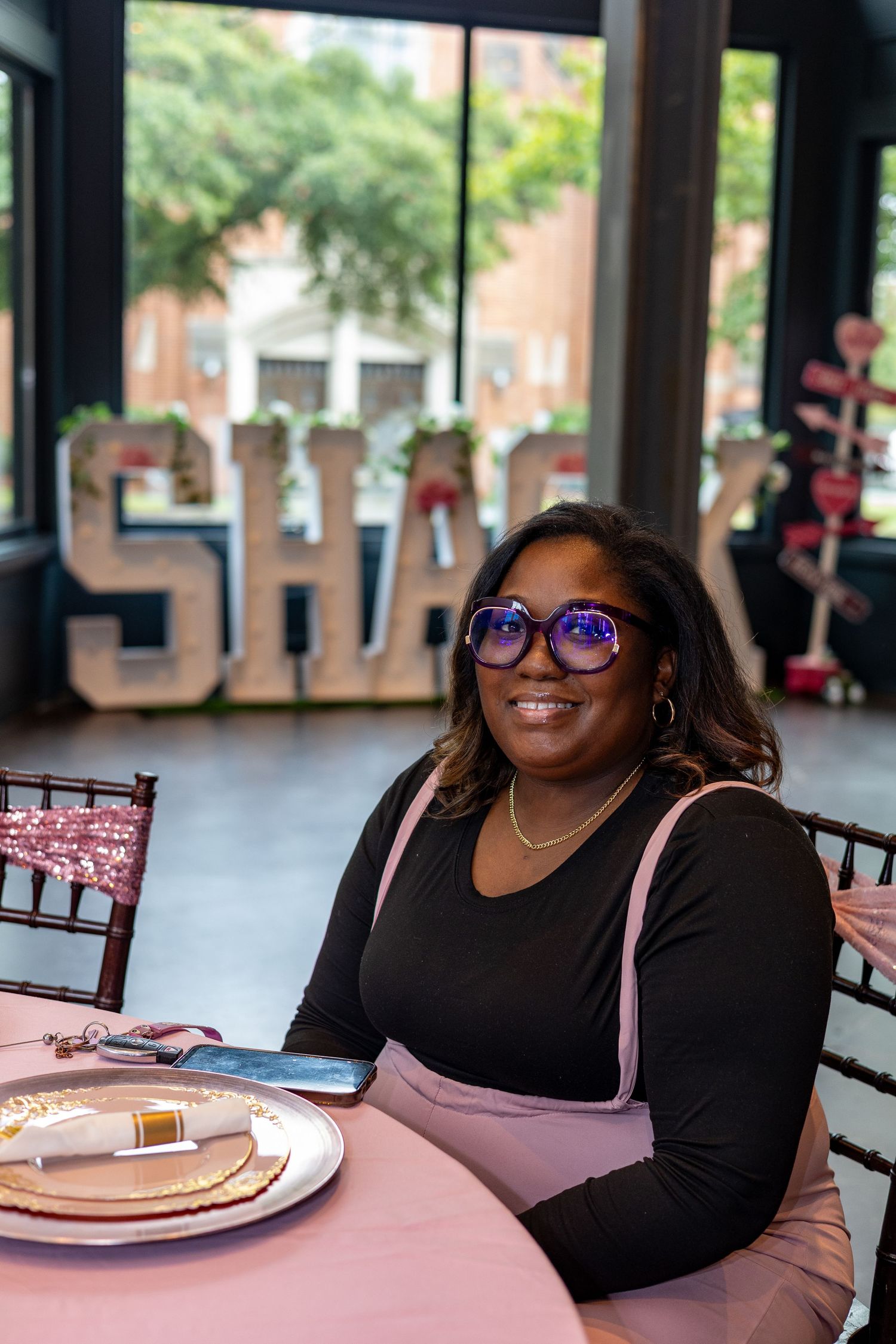 A person wearing glasses sits at a table in a restaurant setting with plates and dining decor visible.