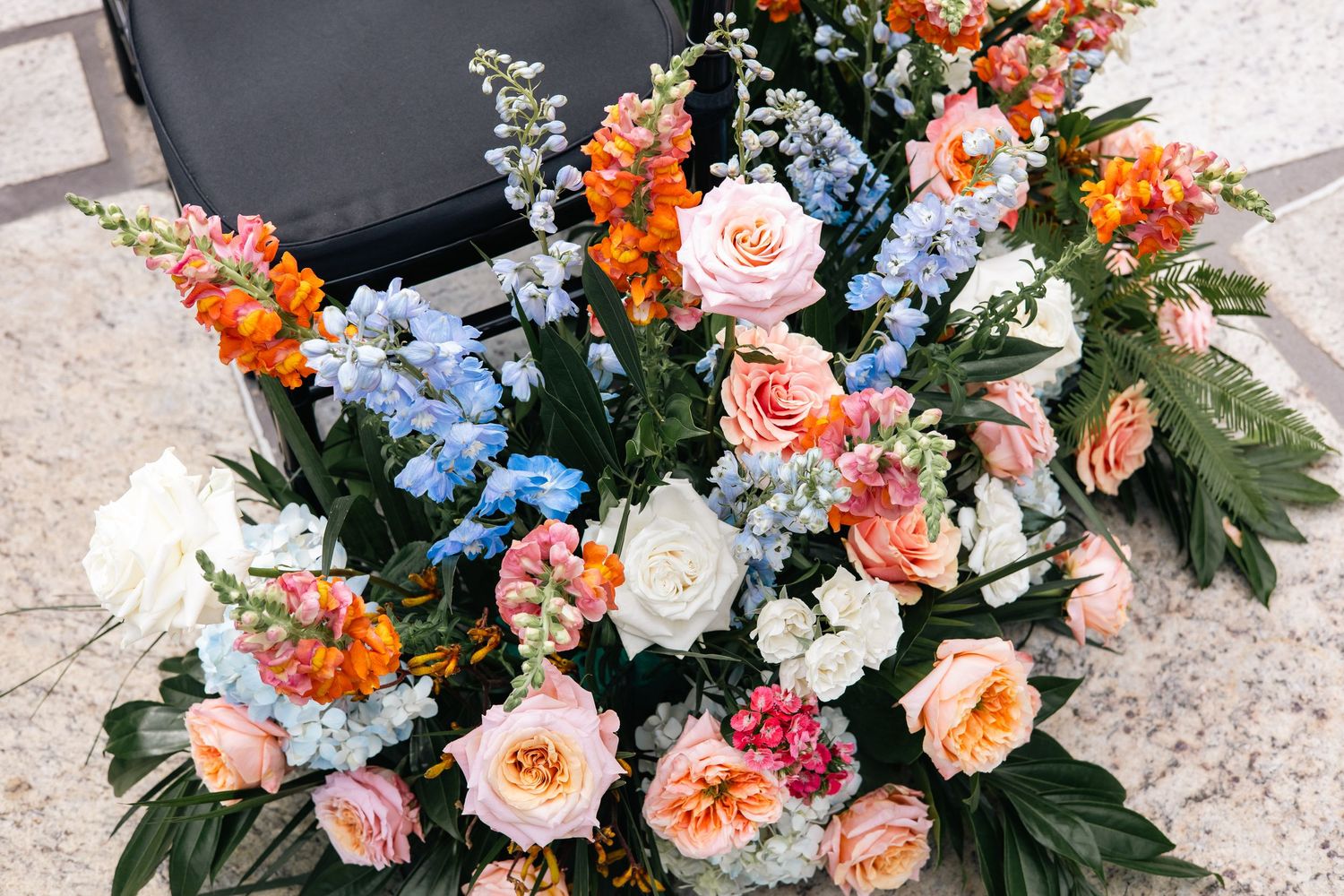 Beautiful floral arrangement featuring peach roses, orange blossoms, and blue delphinium in a garden-inspired design.