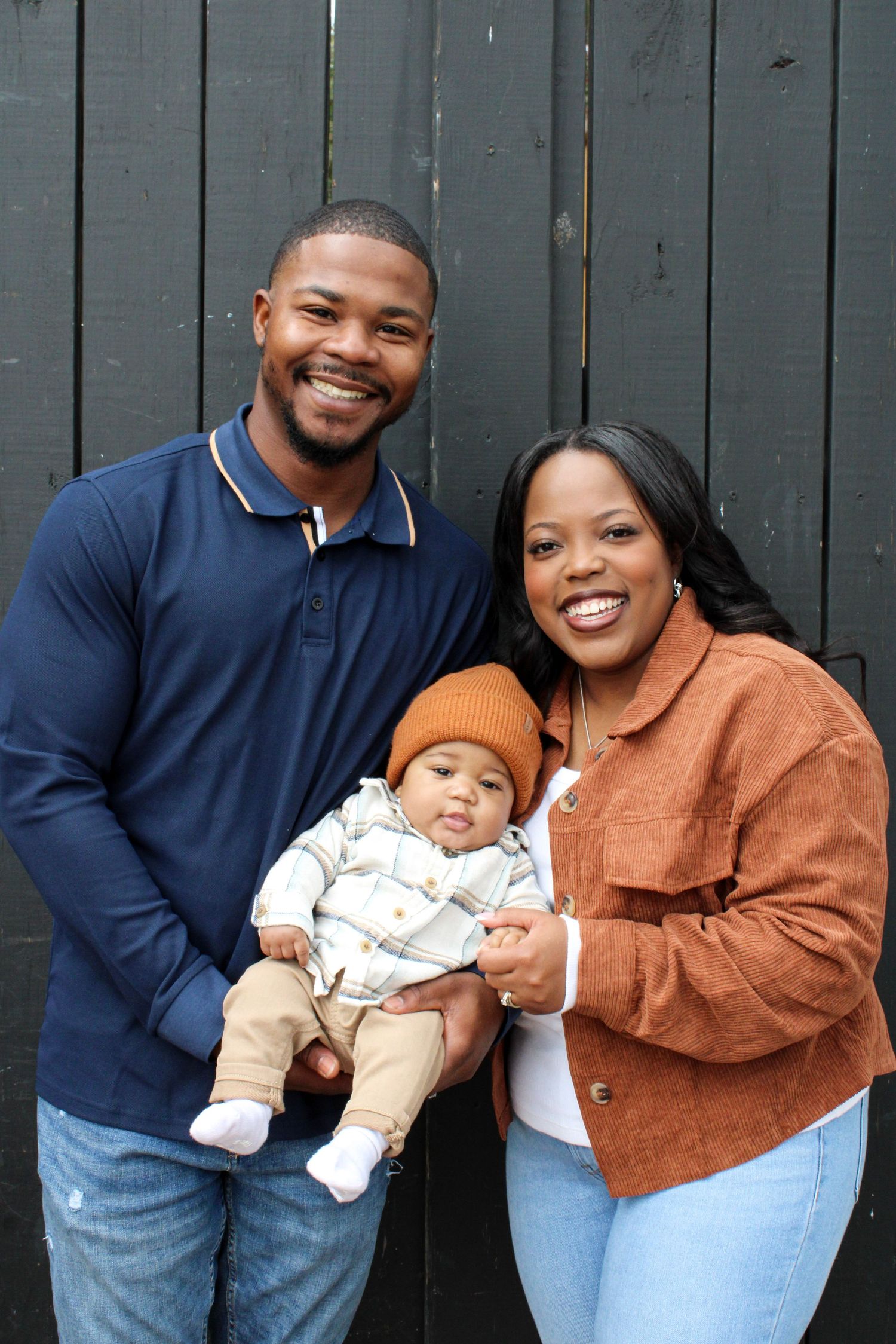 Happy family poses together against grey fence background for outdoor portrait.