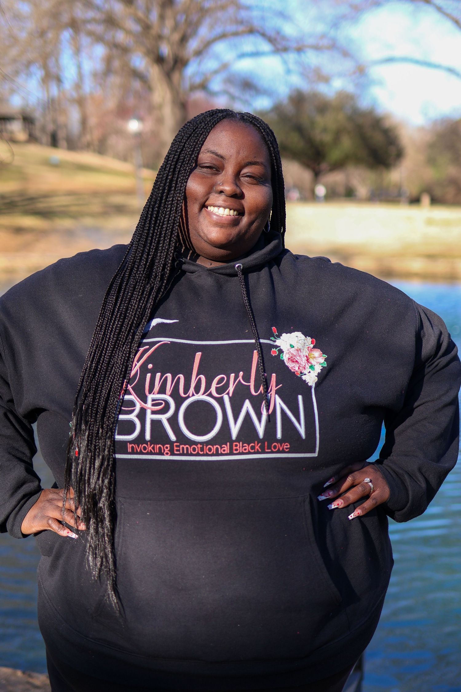 Series of black sweatshirts with different text designs displayed against a lake backdrop on a sunny day.