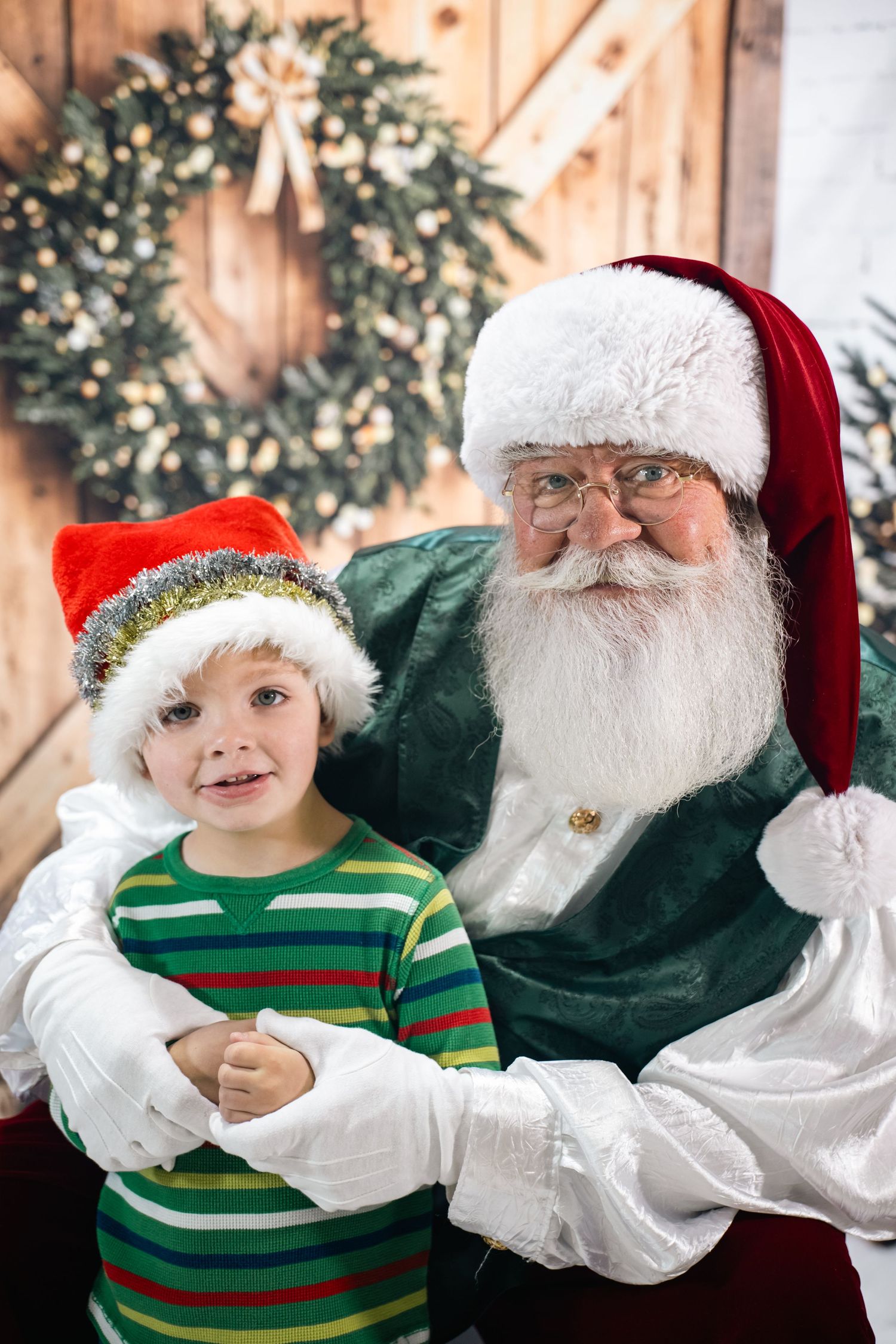 A festive holiday scene with a decorated wreath and traditional Christmas figures in front of a wooden wall.