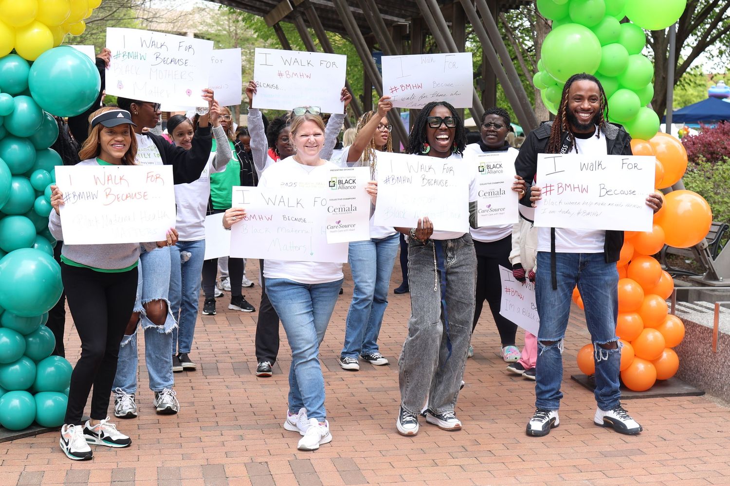 Demonstrators hold signs while marching during rally with colorful balloon decorations.