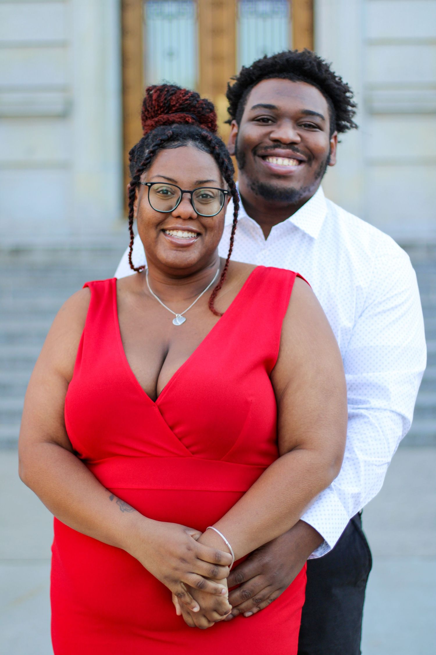 A couple poses in formal wear on steps, with a stunning red dress and crisp white shirt.