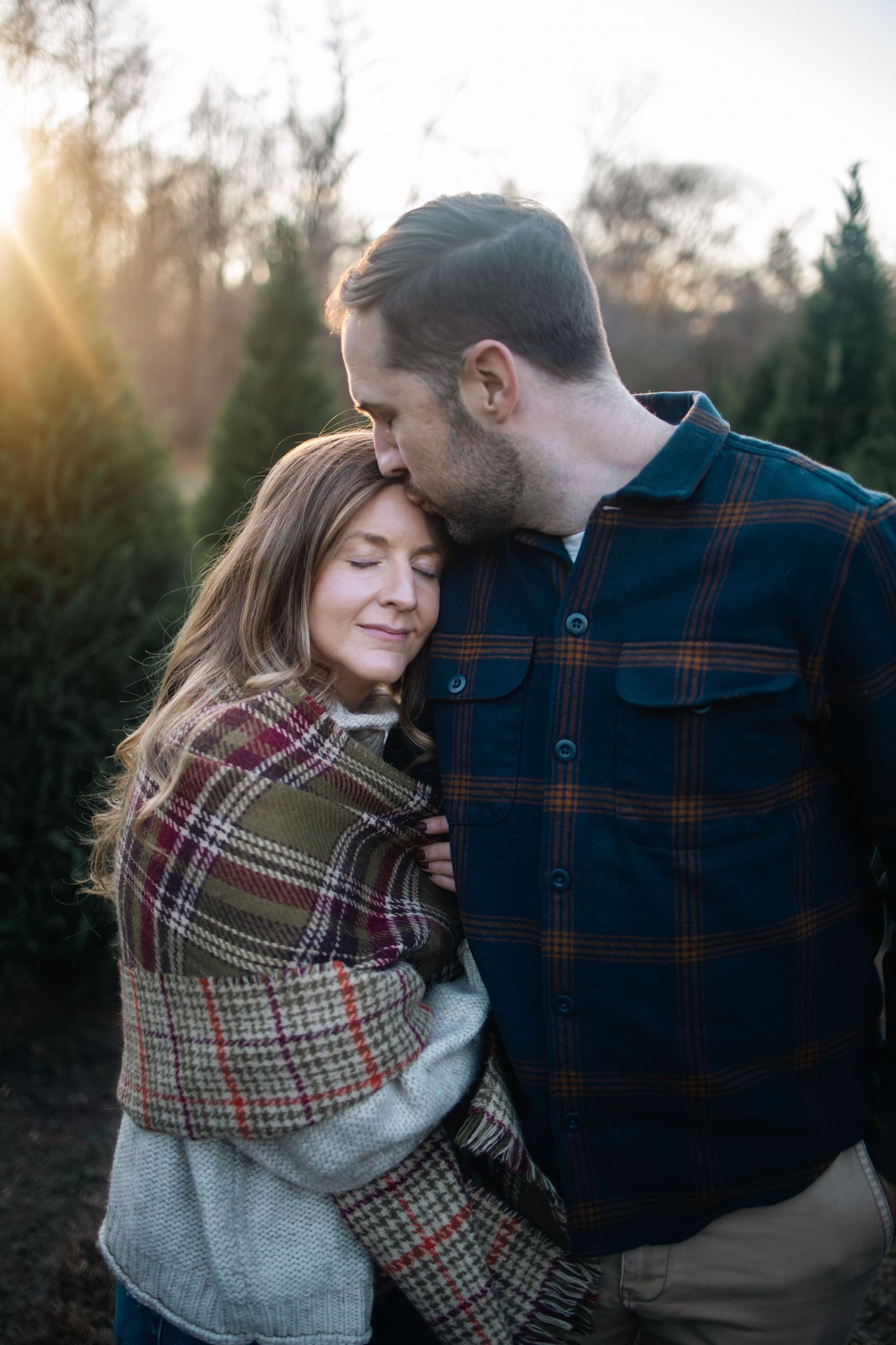 A romantic outdoor portrait of a couple embracing in plaid flannel shirts during golden hour sunset.
