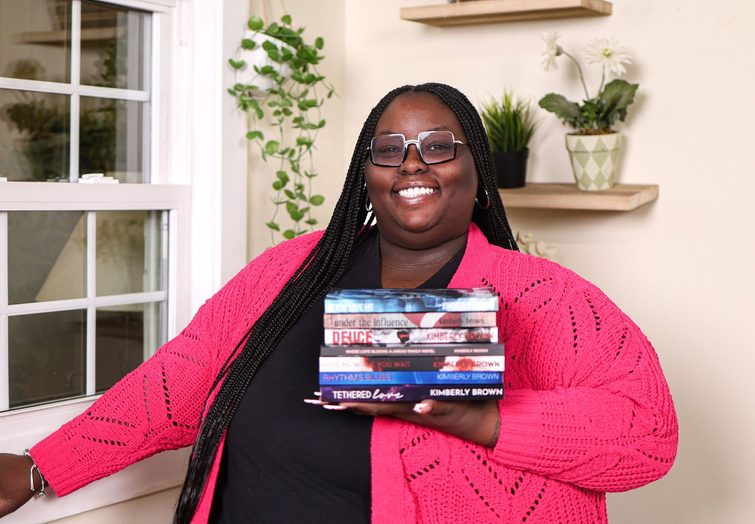 A collage of five photos showing someone in a bright pink sweater posing with books and smiling warmly.
