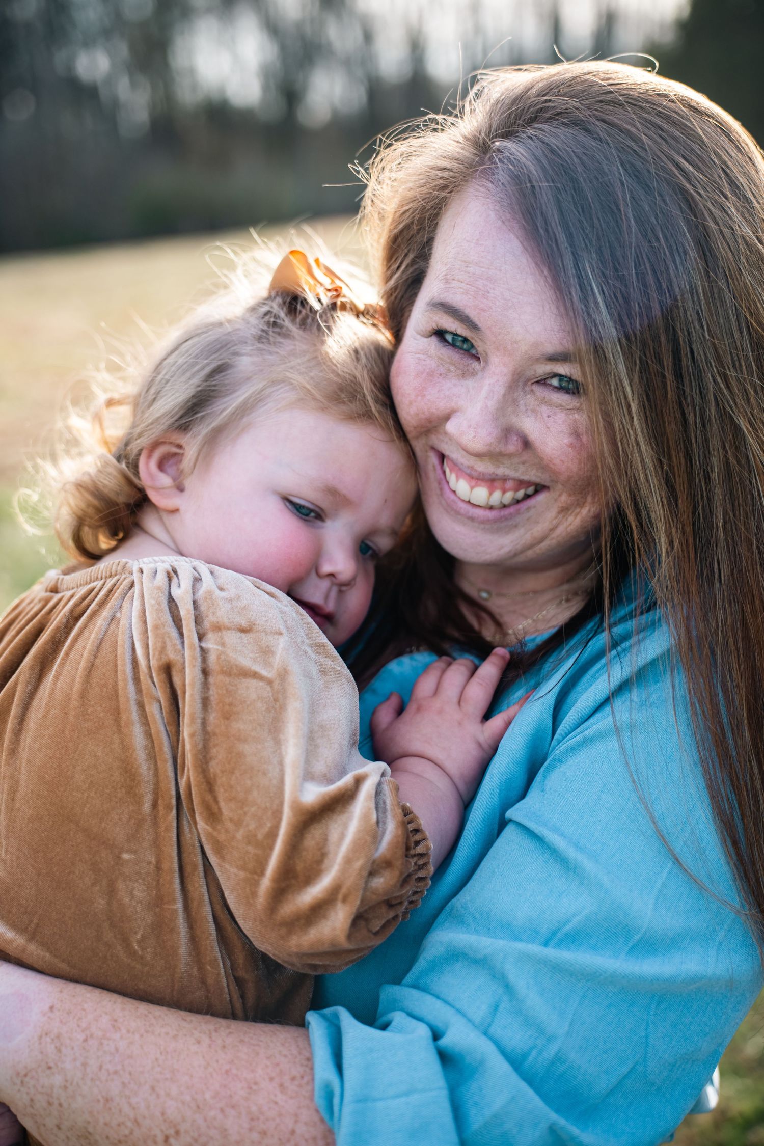 A tender moment captured outdoors with warm sunlight creating a backlit glow during an embrace.