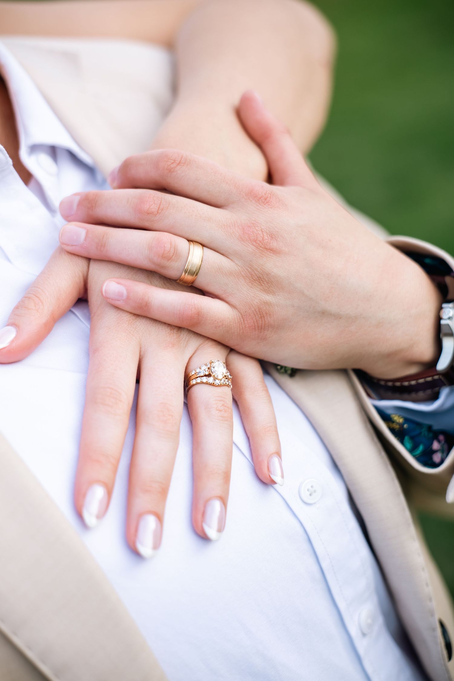 Close-up of couple's hands showing gold wedding band and diamond engagement ring resting on white shirt.
