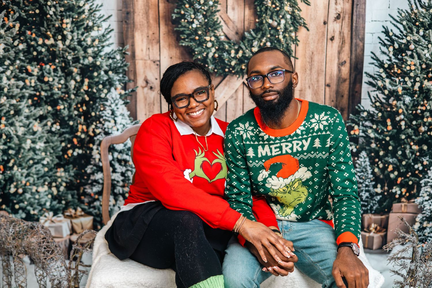 A family wearing coordinated holiday outfits poses together against a festive backdrop with Christmas trees.