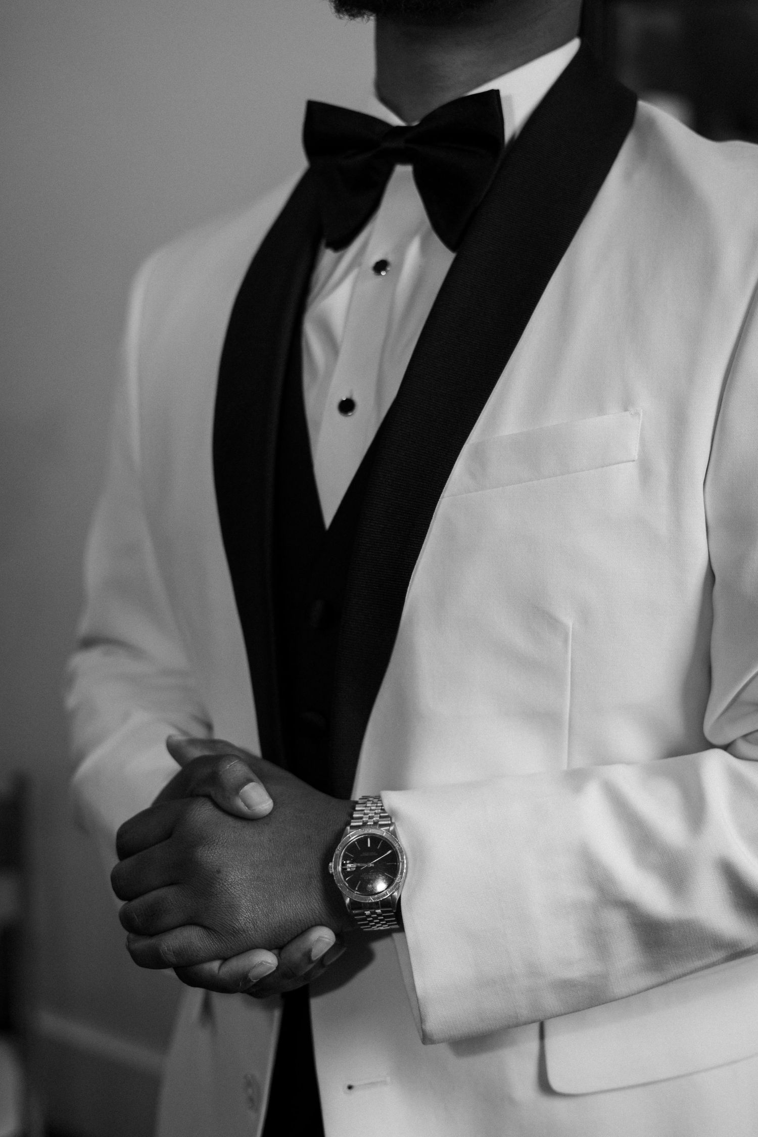 Close-up details of a formal white tuxedo jacket with black lapels and a silver watch visible on the wearer's wrist.