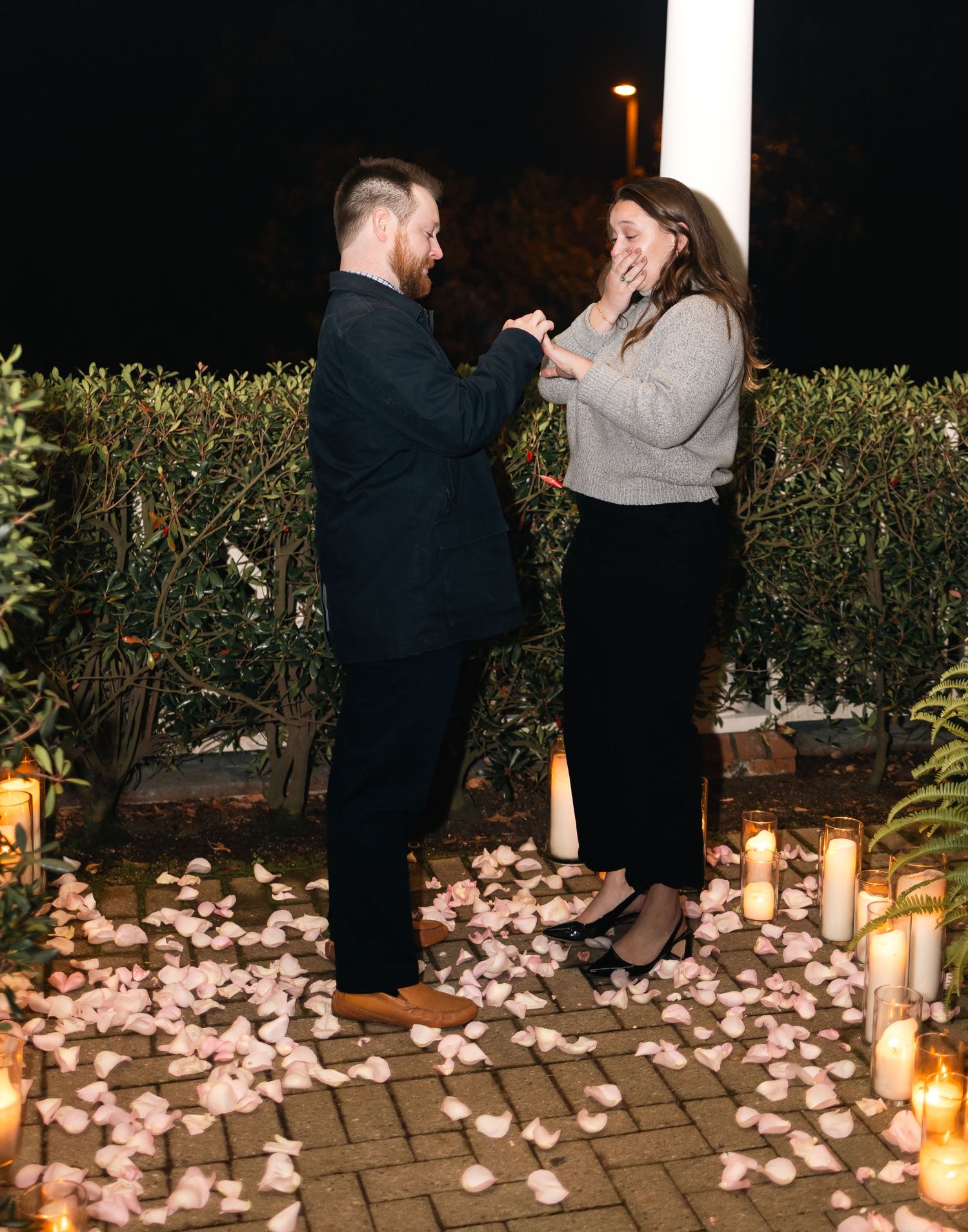 A romantic proposal sequence with candles and rose petals arranged on a stone patio at night.