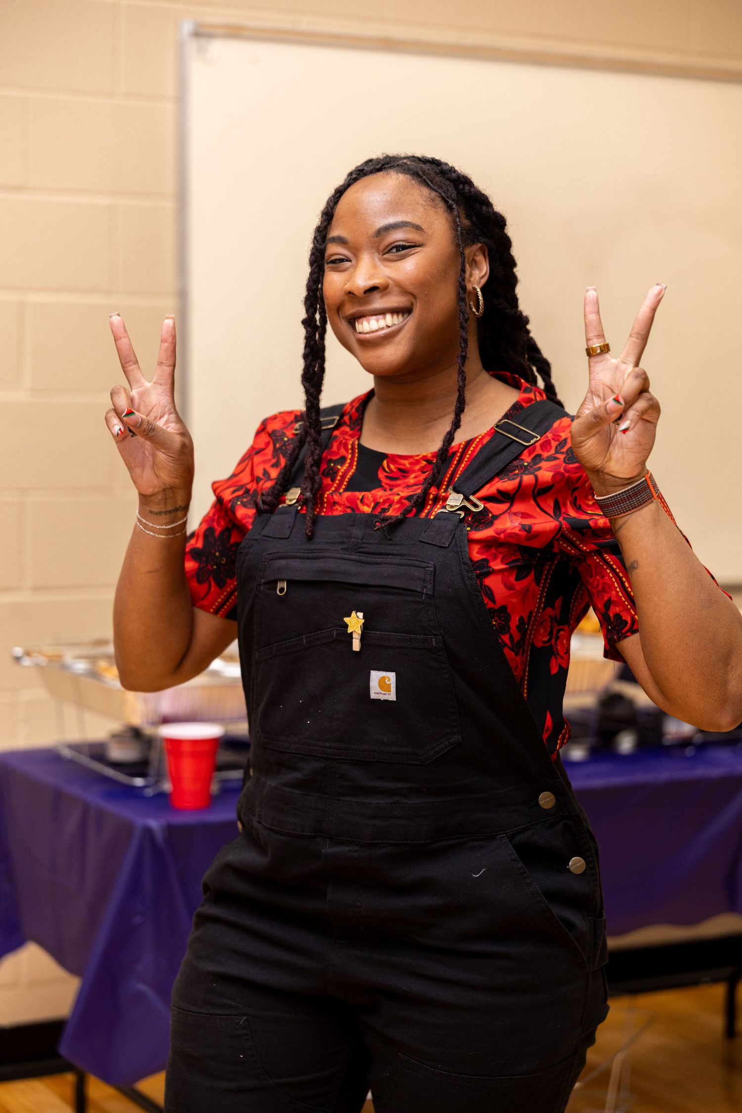 A person in black overalls and red ruffled sleeves makes peace signs while smiling in a sequence of four photos.