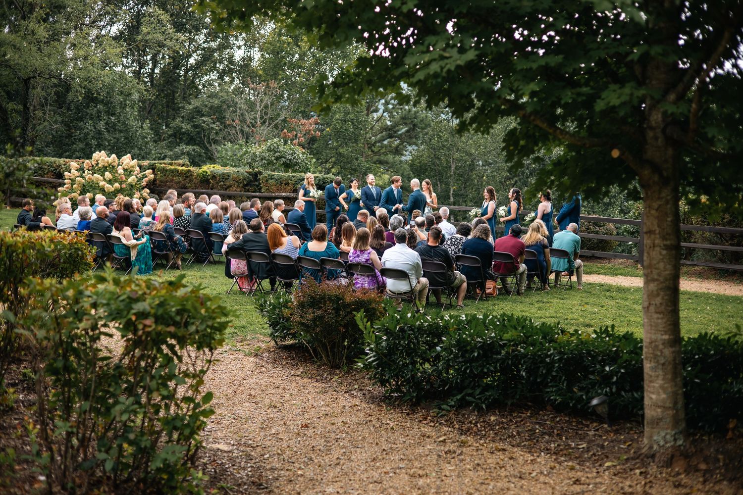 A large crowd of people gathered outdoors under trees for a special event or celebration.