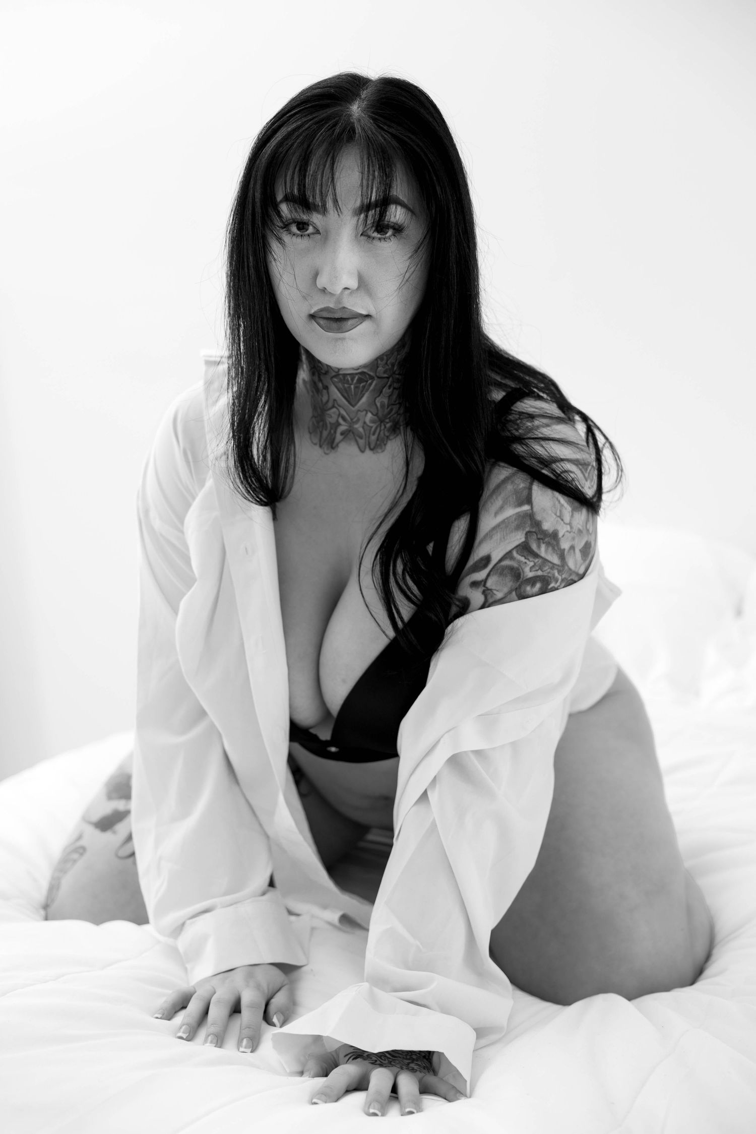 Artistic boudoir photo of tattooed model wearing white shirt on light background.