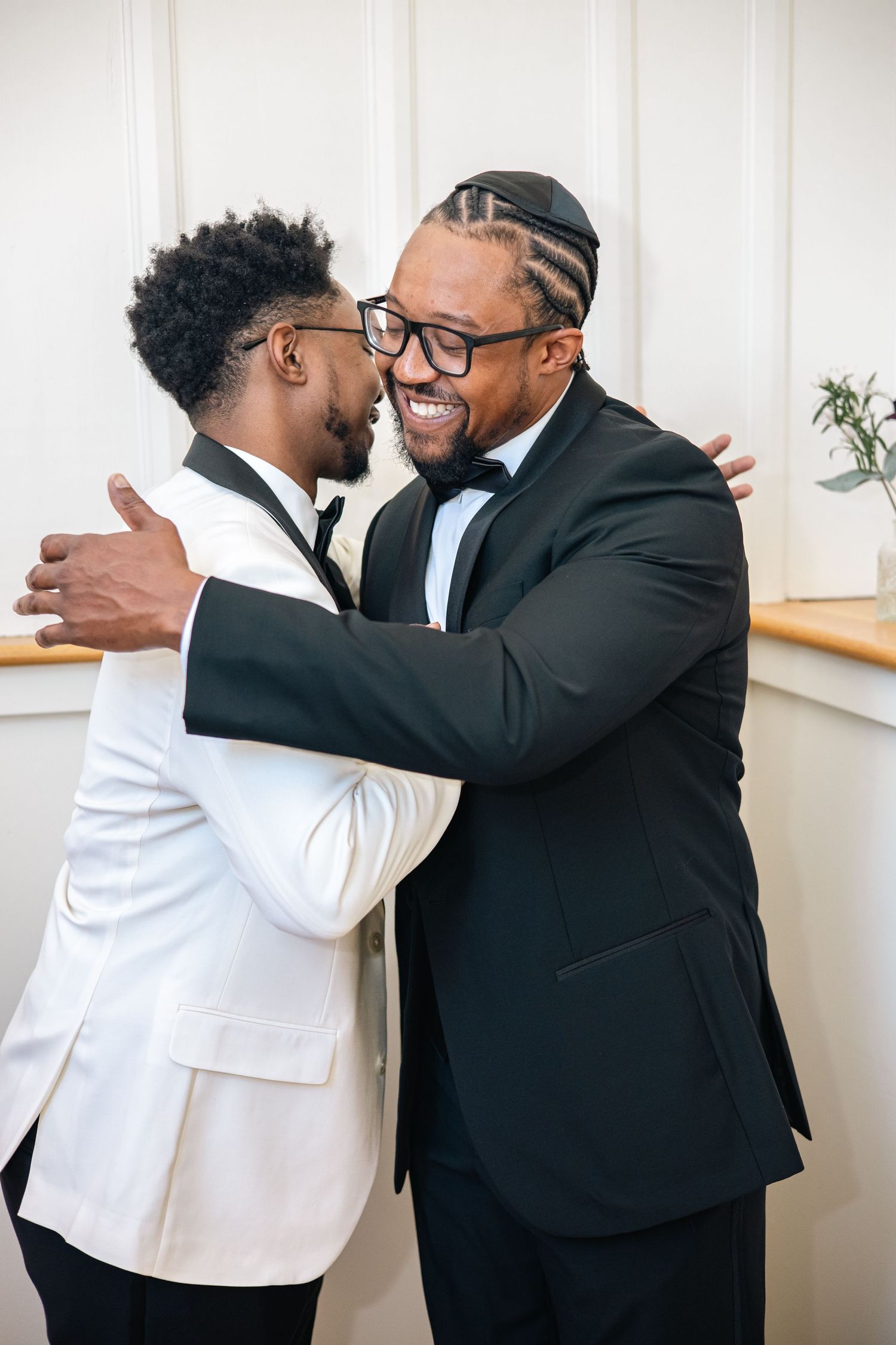 A series of emotional embraces between two people wearing black and white formal attire against a white wall.