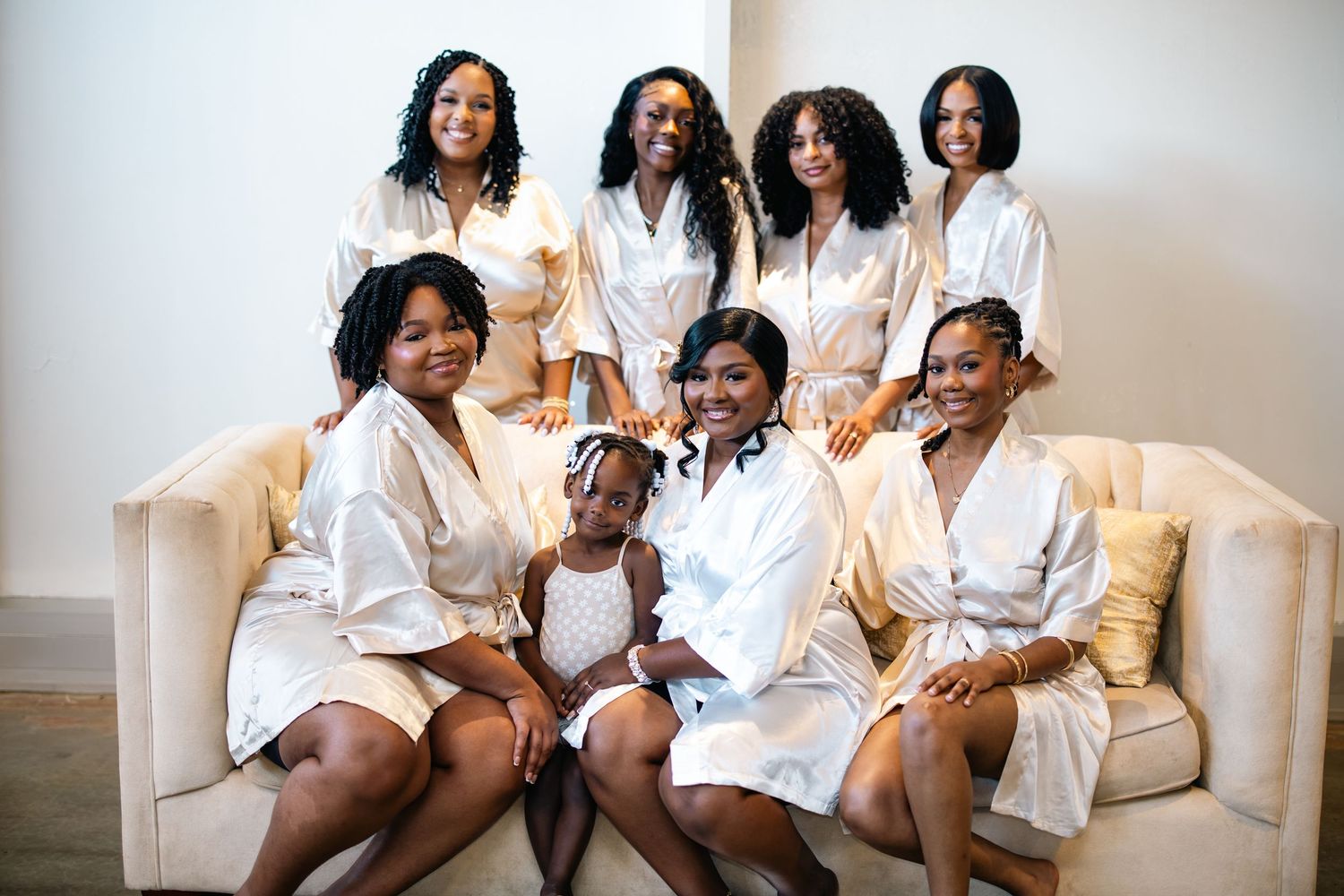 A group wearing white robes sits together on a cream colored couch in a bright room.