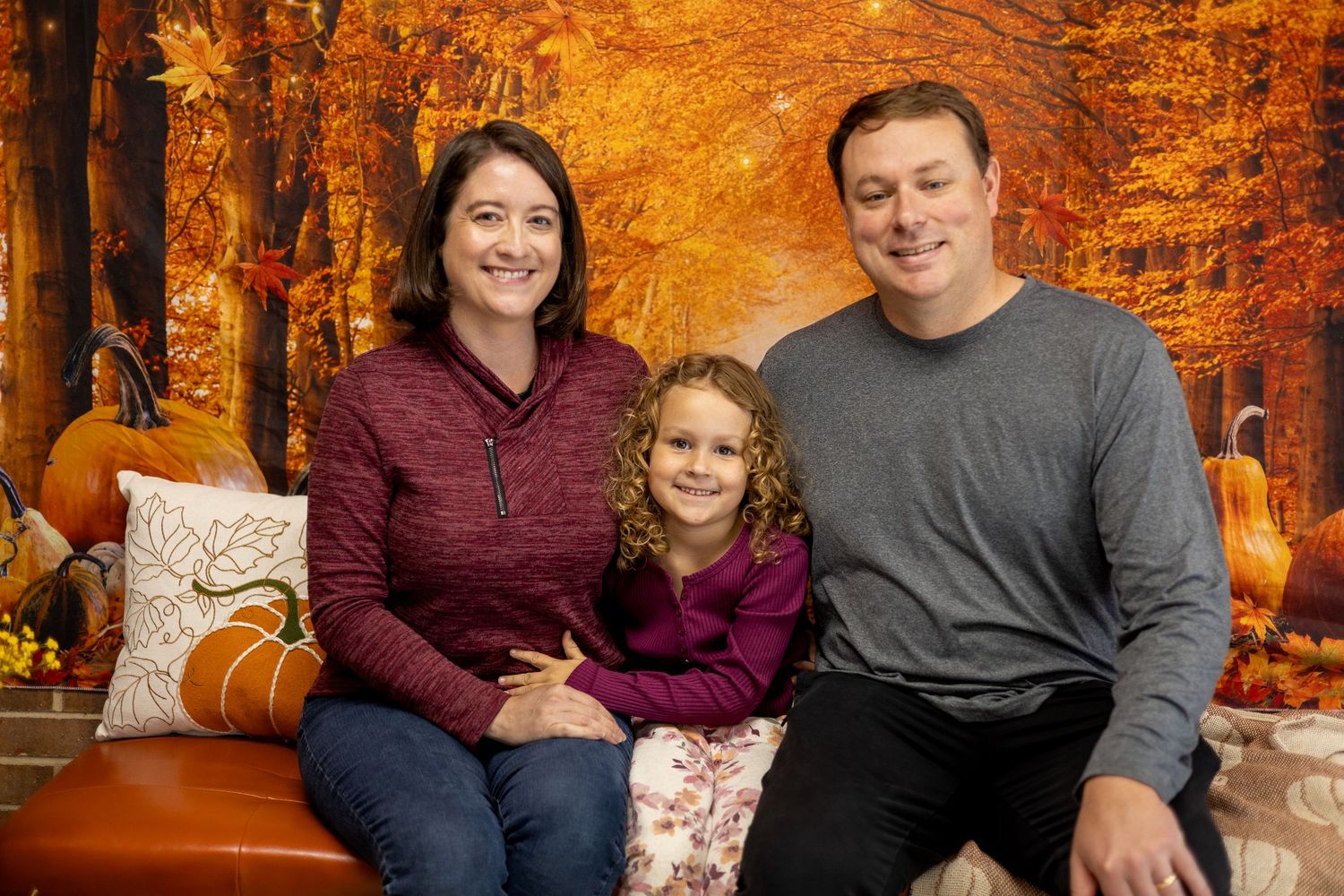 A family poses together for autumn portraits with pumpkins and fall foliage in warm orange tones.