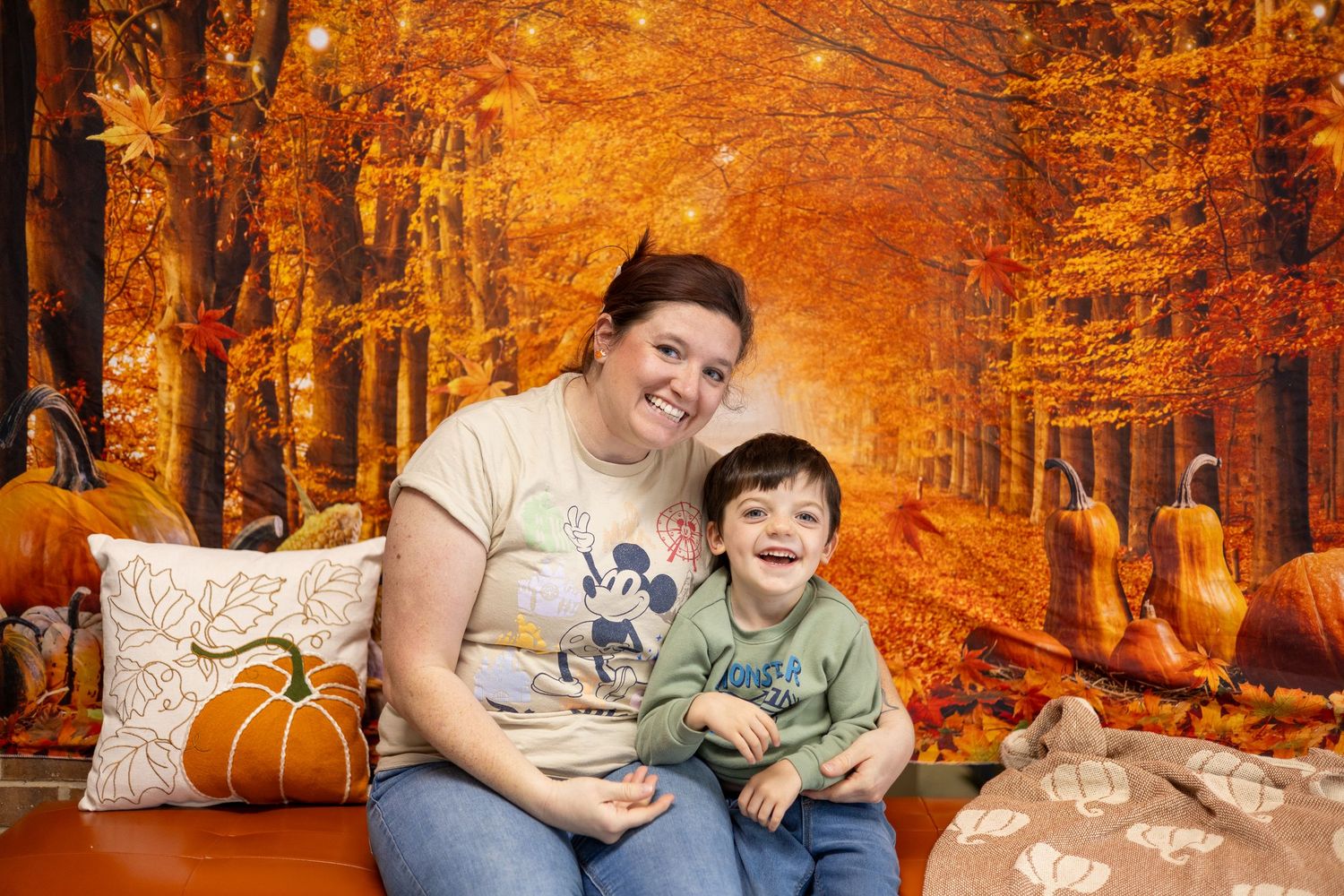 A cozy autumn portrait session with decorative pumpkins and a warm orange forest backdrop.