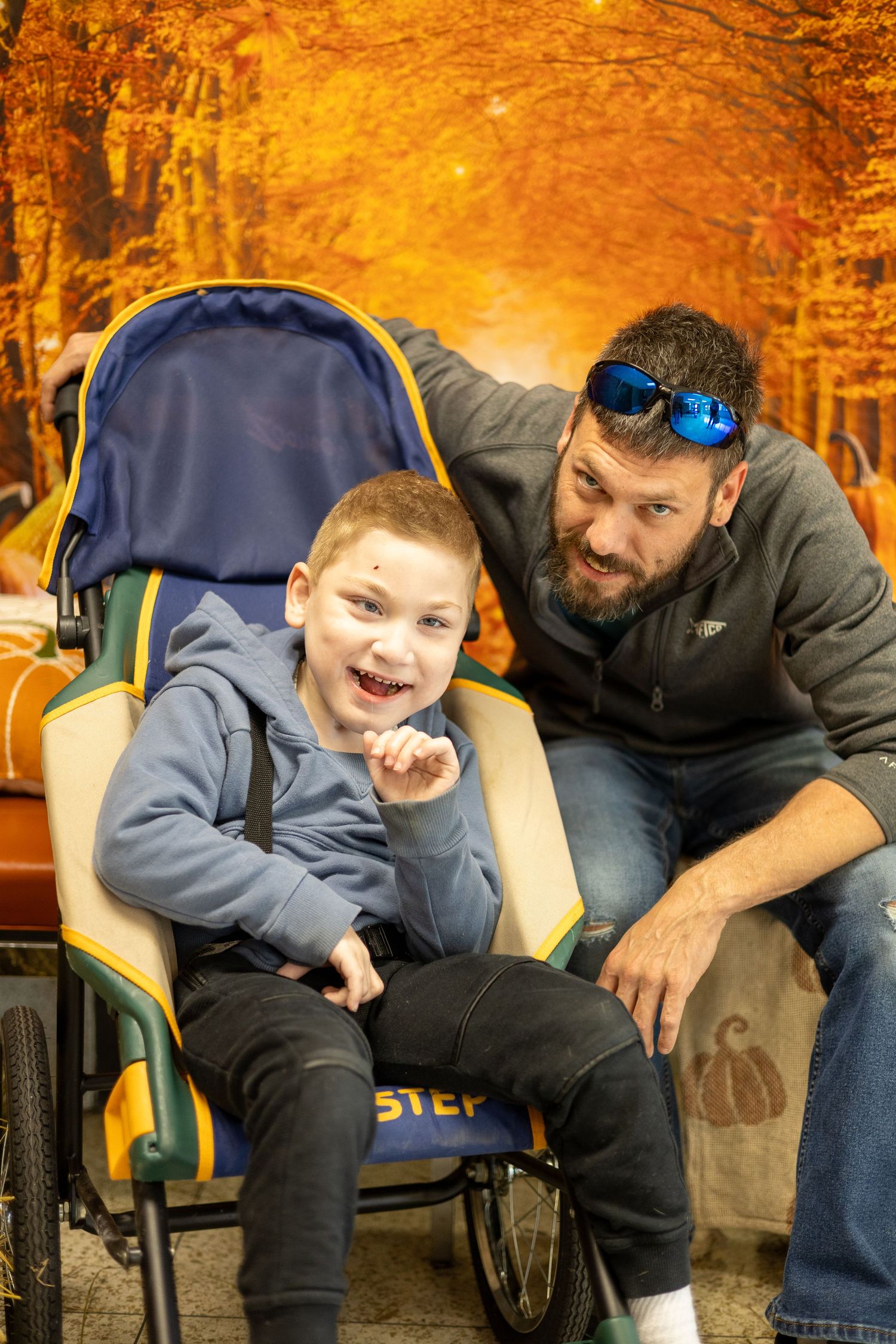 Two people share a playful moment while sitting on chairs in a park with golden autumn foliage in the background.