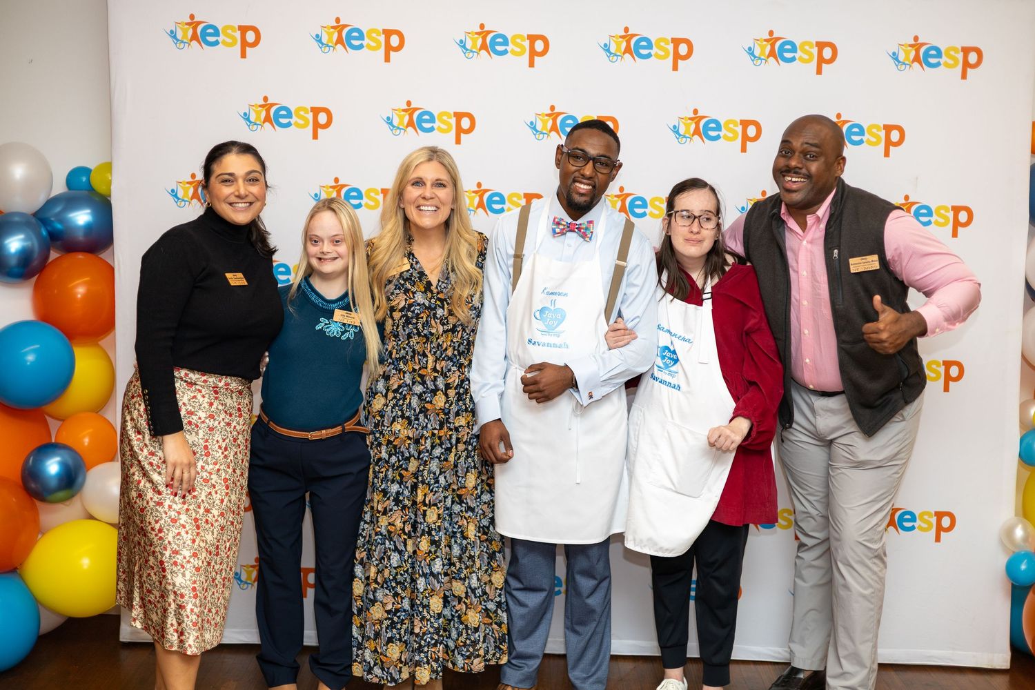 Group of six people smiling together at a KEEP program event, with colorful balloons in the background.