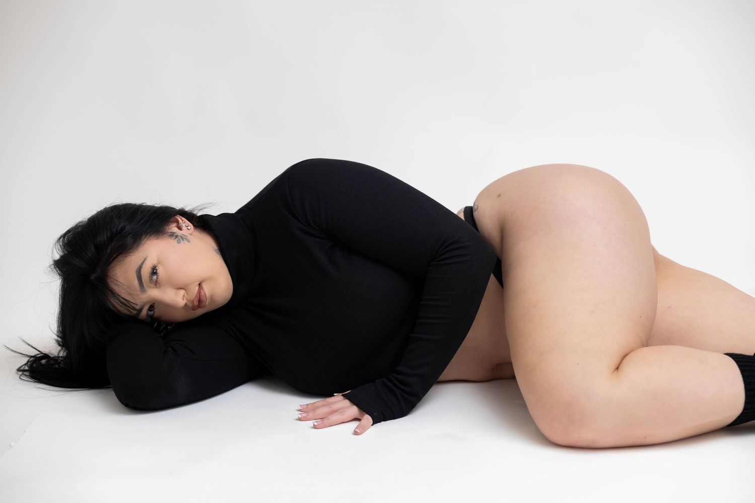 A figure in a black long sleeve top lies gracefully on a white background in a minimalist artistic pose.