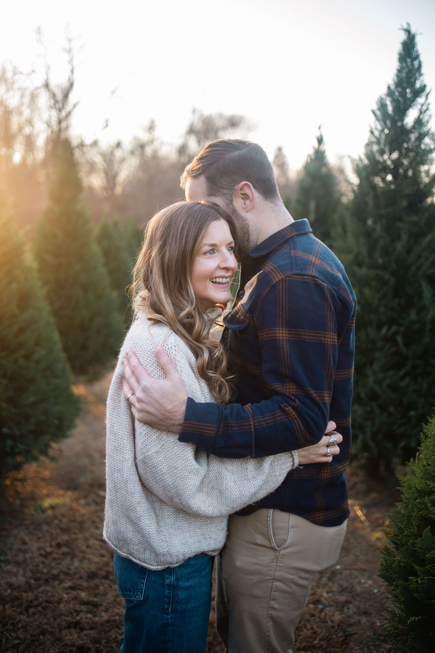 A couple embraces in a Christmas tree farm during a golden sunset photoshoot.