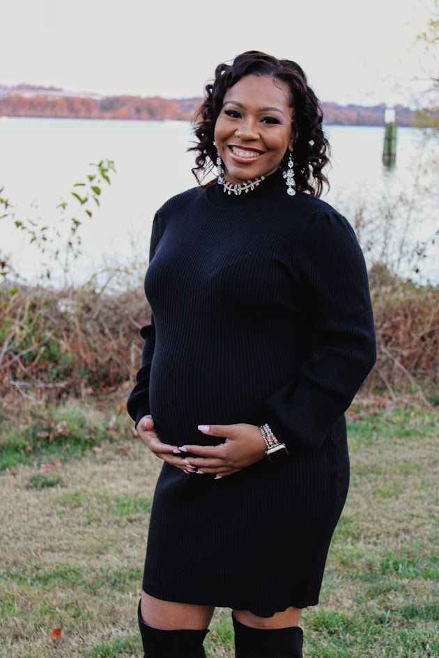 A person wearing a black turtleneck sweater poses outdoors on grass in a maternity photo shoot series.