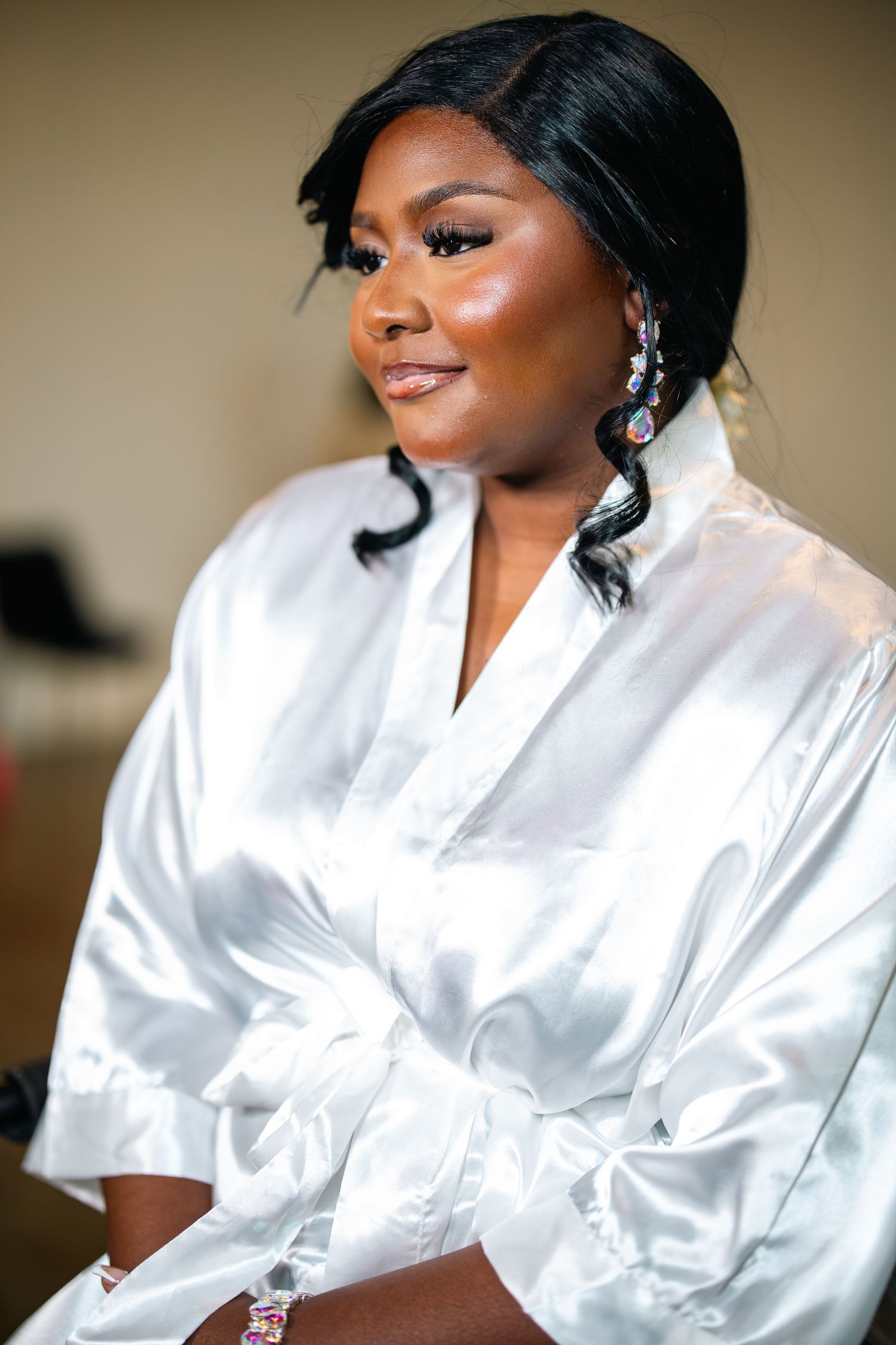 Beautiful person wearing white silk robe glances at camera in wedding day preparation photos.