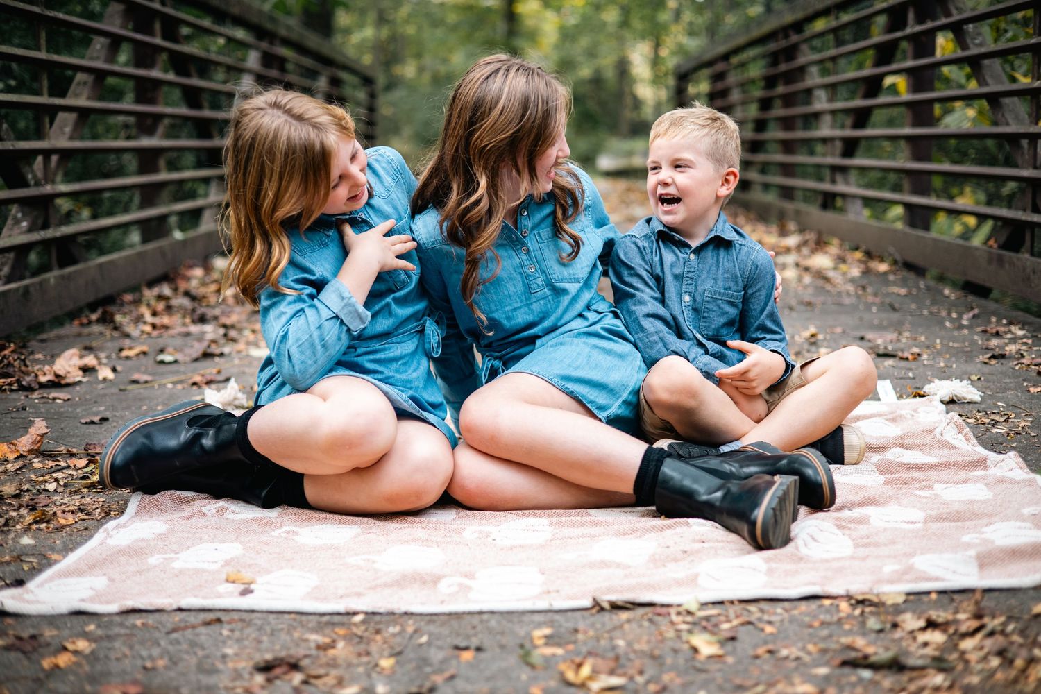 A couple in matching blue outfits laying on a blanket in a wooded area for a romantic photoshoot.