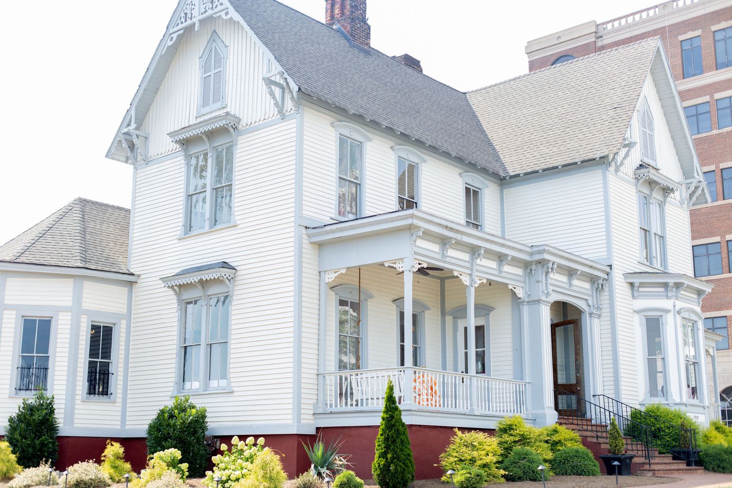 Historic white Victorian house with decorative trim, covered porch, and manicured shrubs in an urban setting.