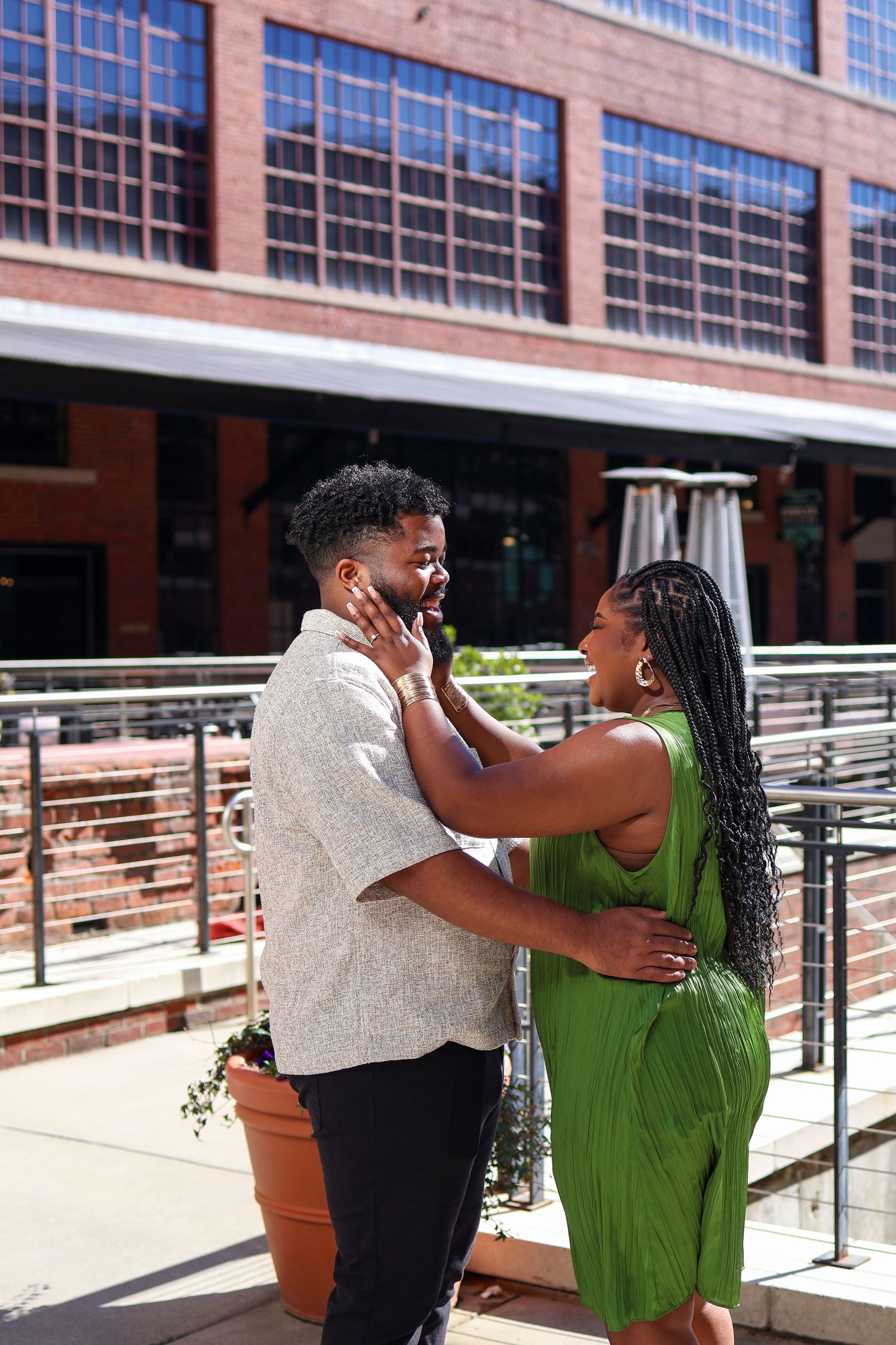 A couple shares a tender moment on an outdoor patio with modern architecture in the background.