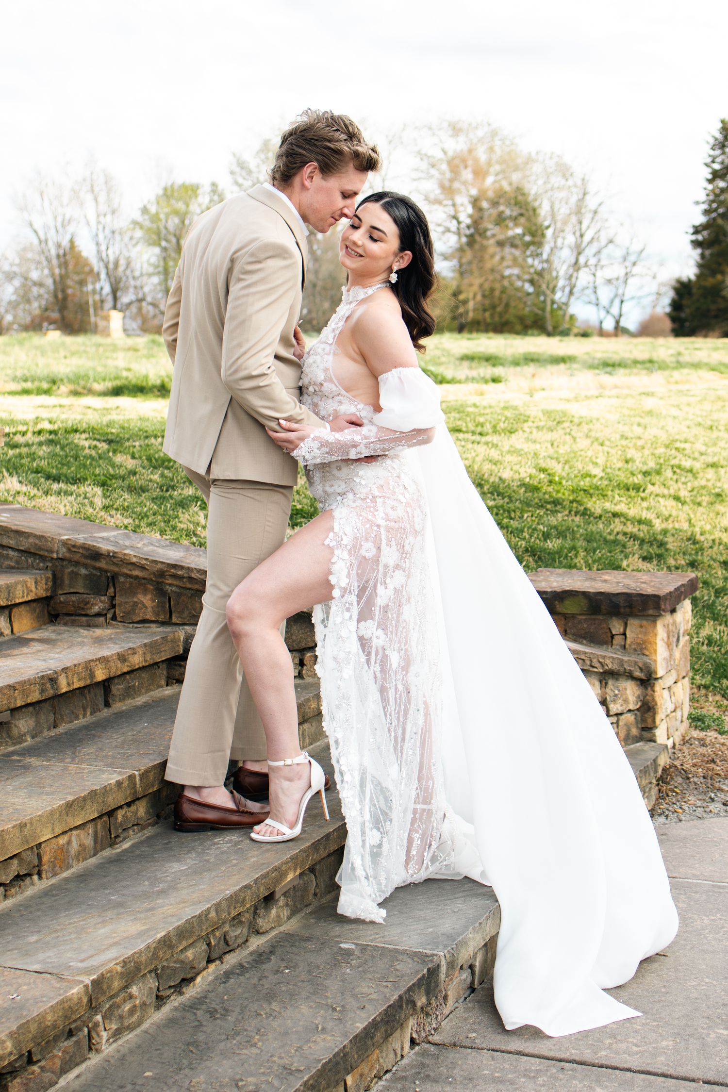 Newlyweds in white dress and tan suit share romantic poses on stone steps outdoors.