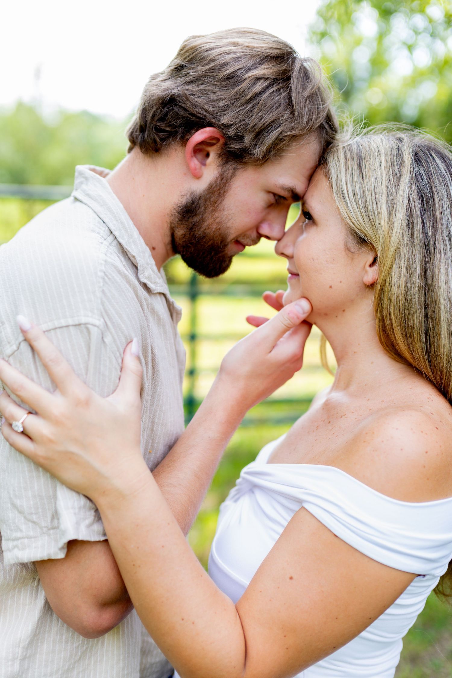 Romantic couple sharing an intimate moment outdoors, touching foreheads gently in a lush green setting.