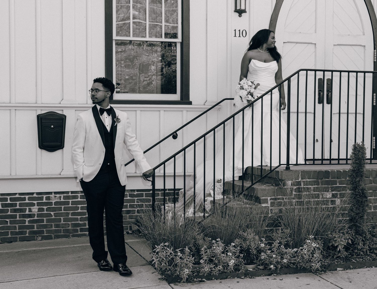 Black and white wedding photo of bride and groom posing separately on steps of building number 110.