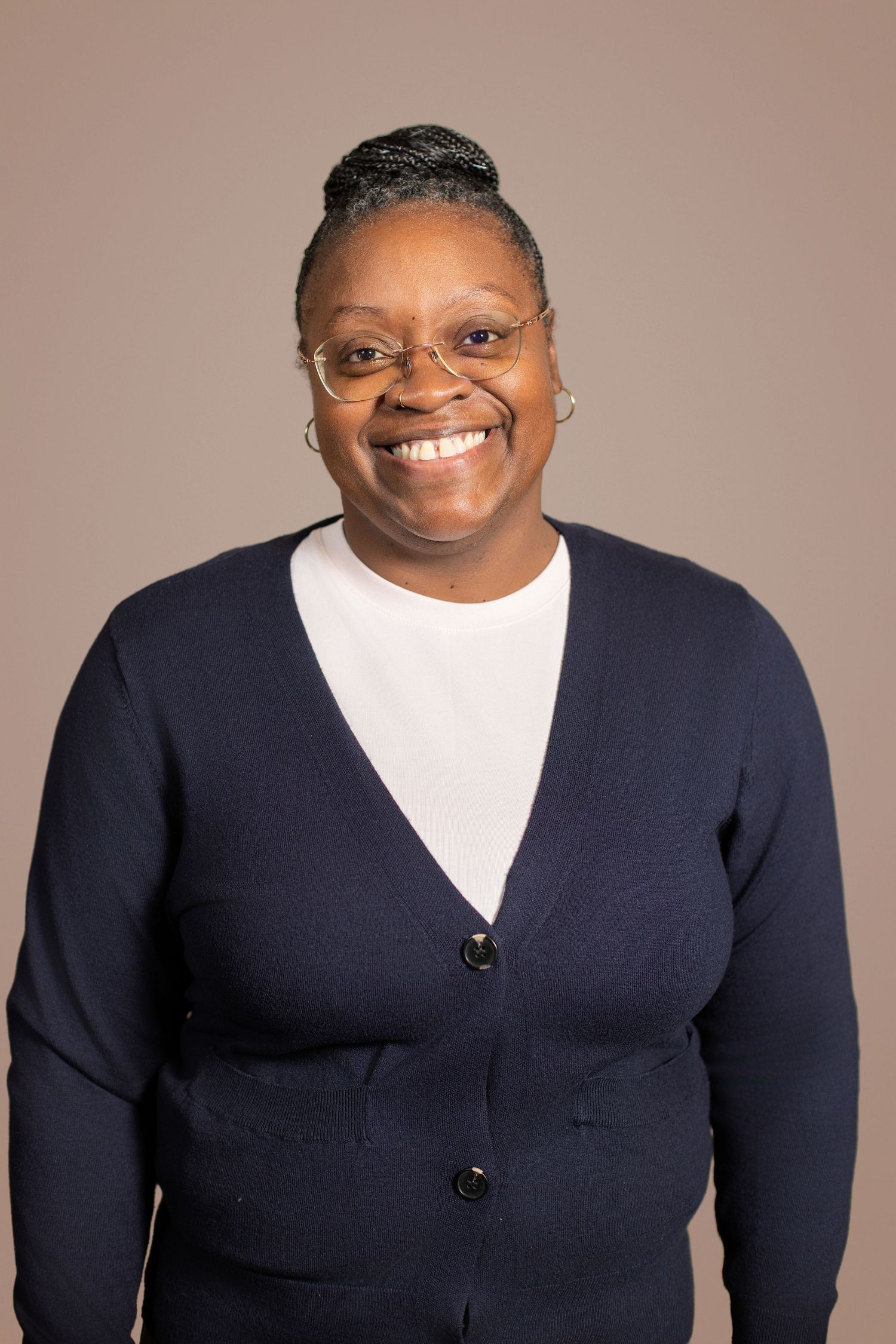Smiling woman wearing glasses and navy cardigan over white shirt poses for professional portrait photo.