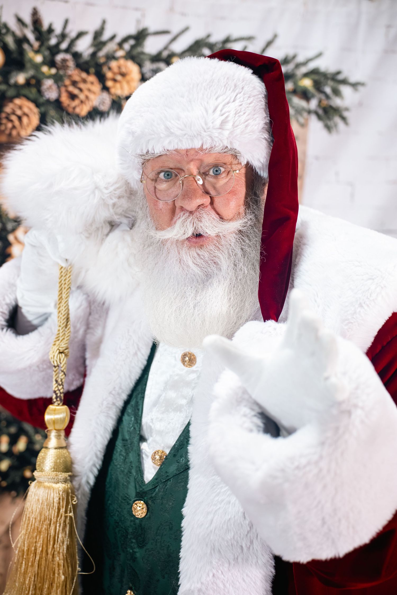 Close-up portrait of a traditional Santa Claus figure wearing a red velvet hat and green vest against a festive background.