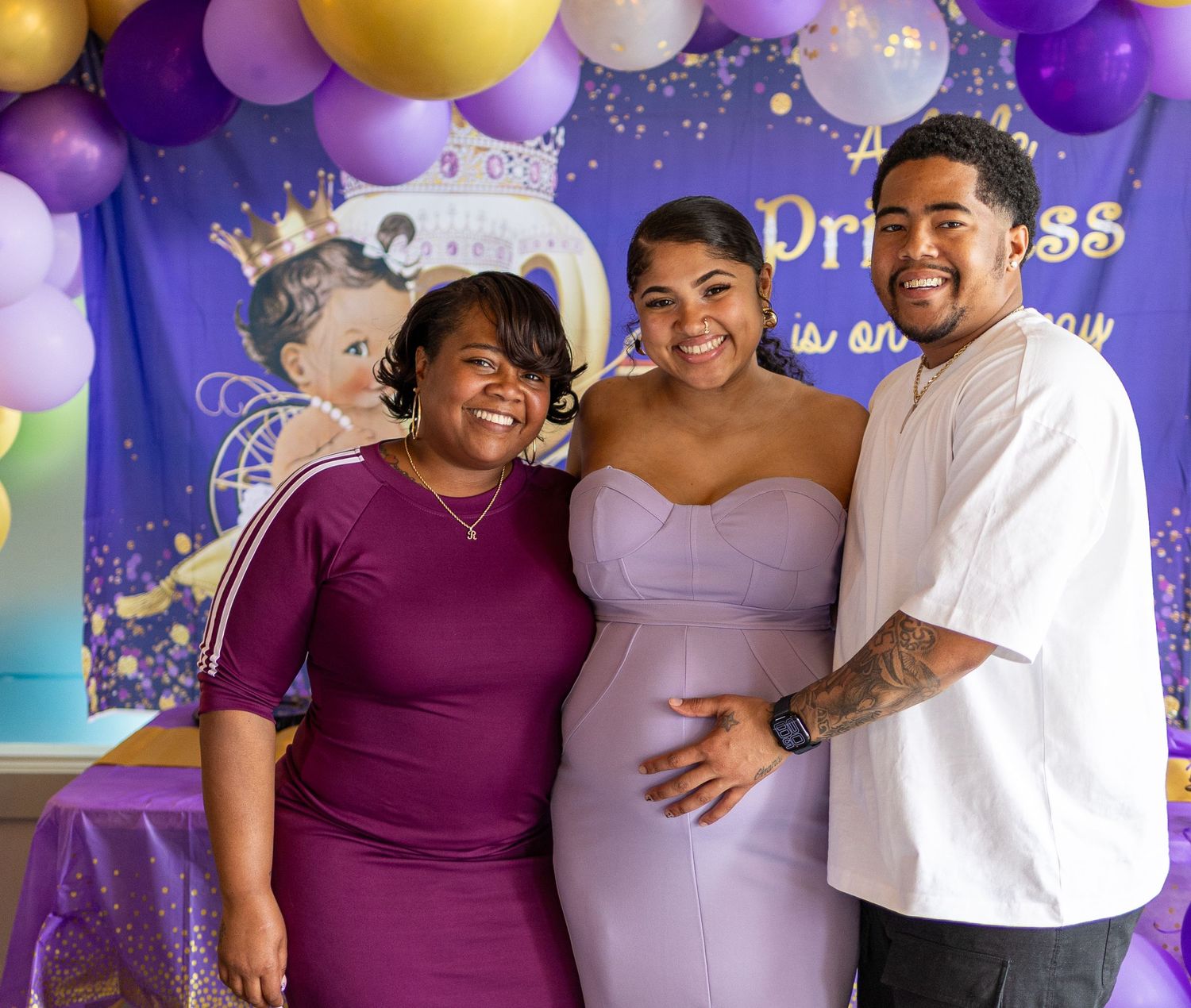 Family gathering at princess-themed baby shower with purple and gold balloon decorations.