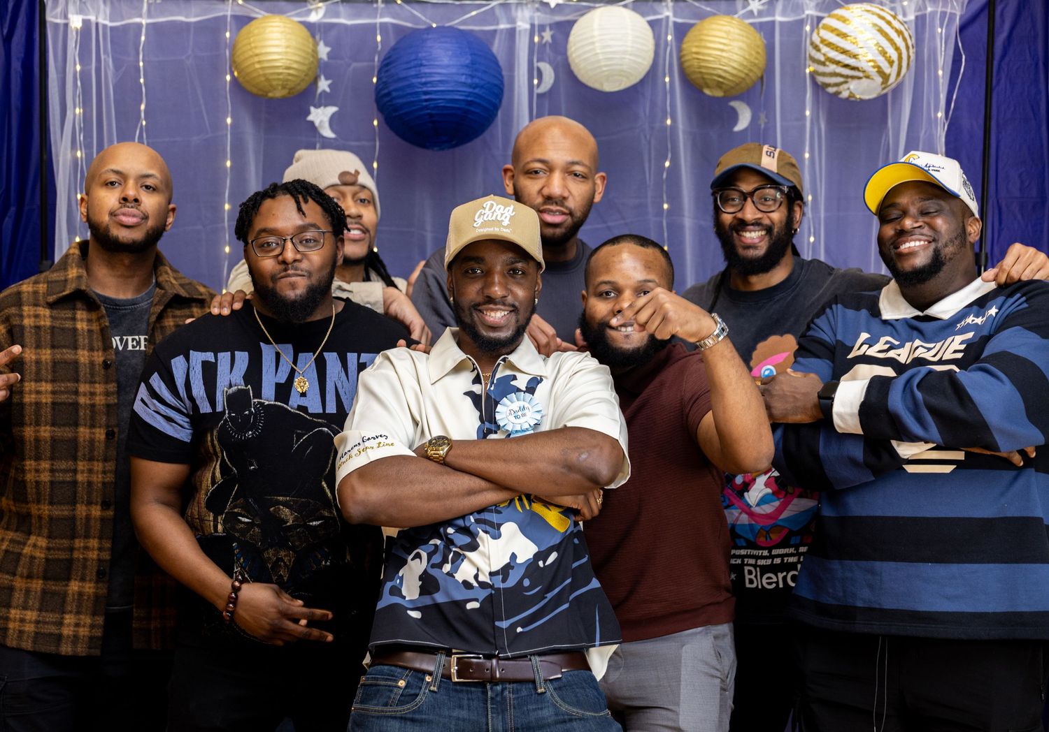 A group poses together at a party decorated with blue and gold balloons and hanging streamers.