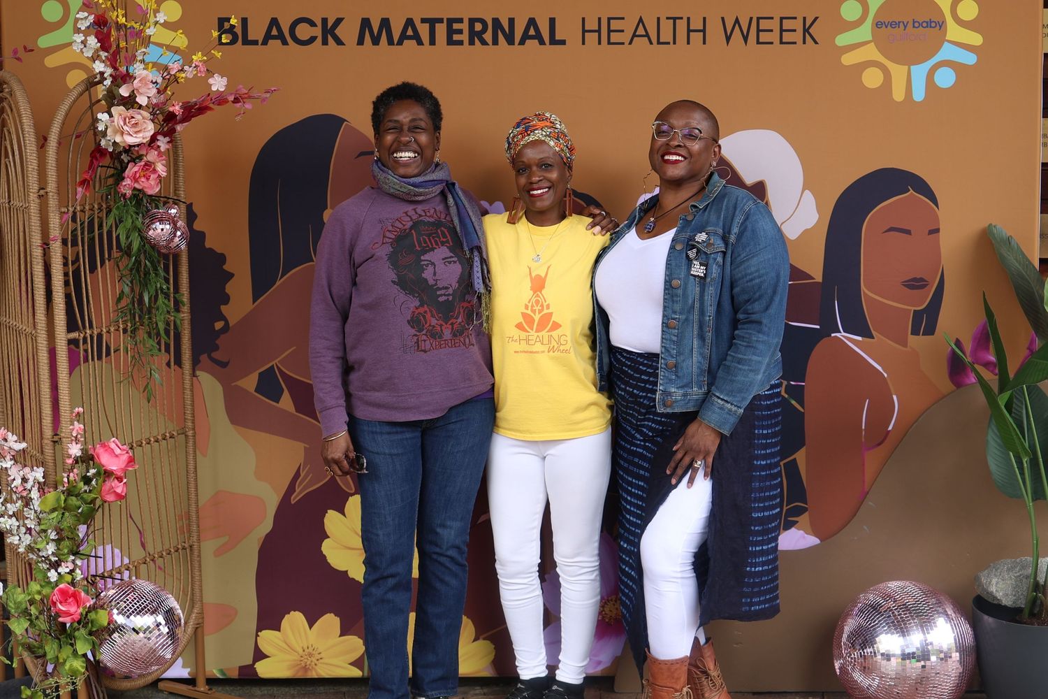 Group photo at Black Maternal Health Week event with decorative backdrop and florals.