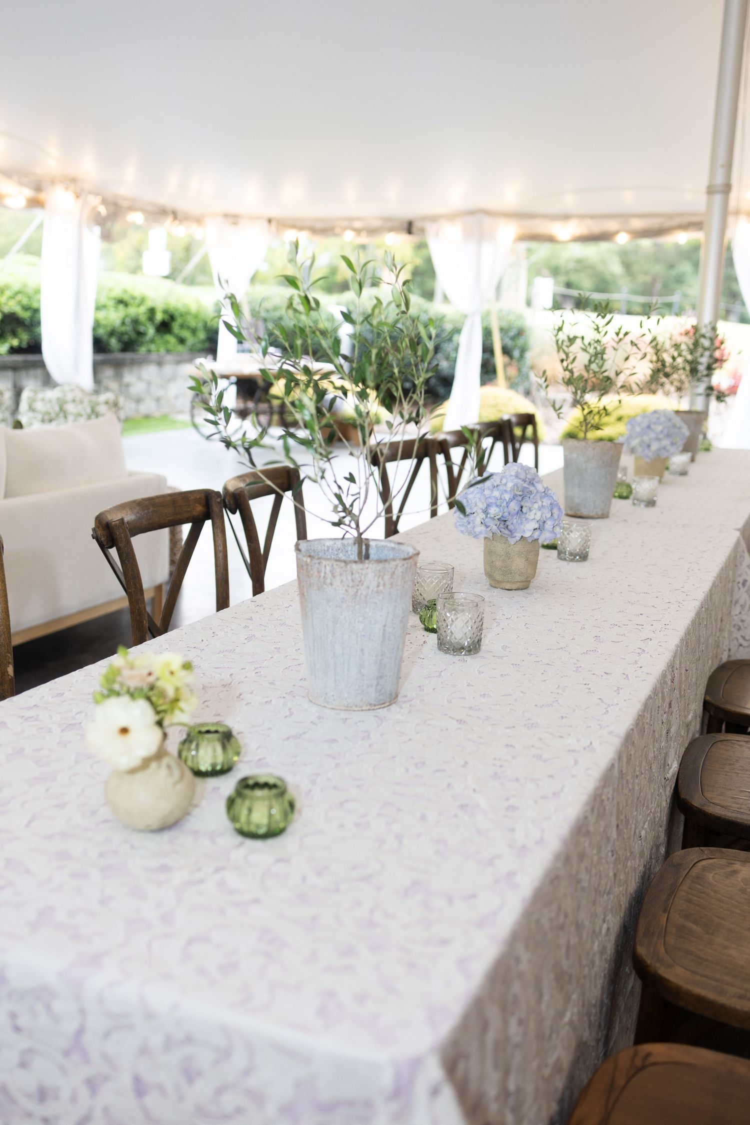 Long reception tables set with white linens and delicate floral centerpieces under an outdoor tent.
