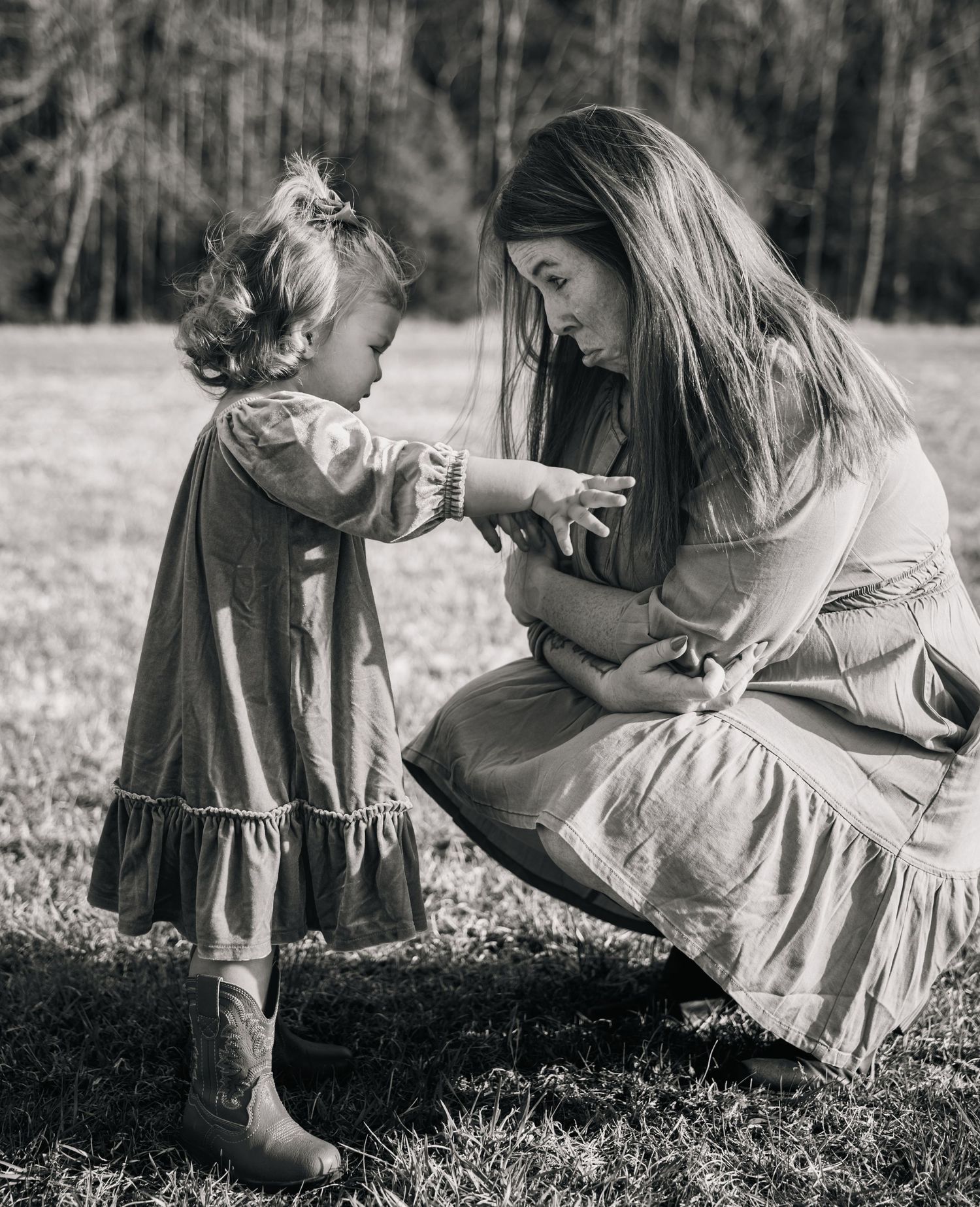 Black and white photos show tender outdoor moments between parent and child sitting in a grassy field.