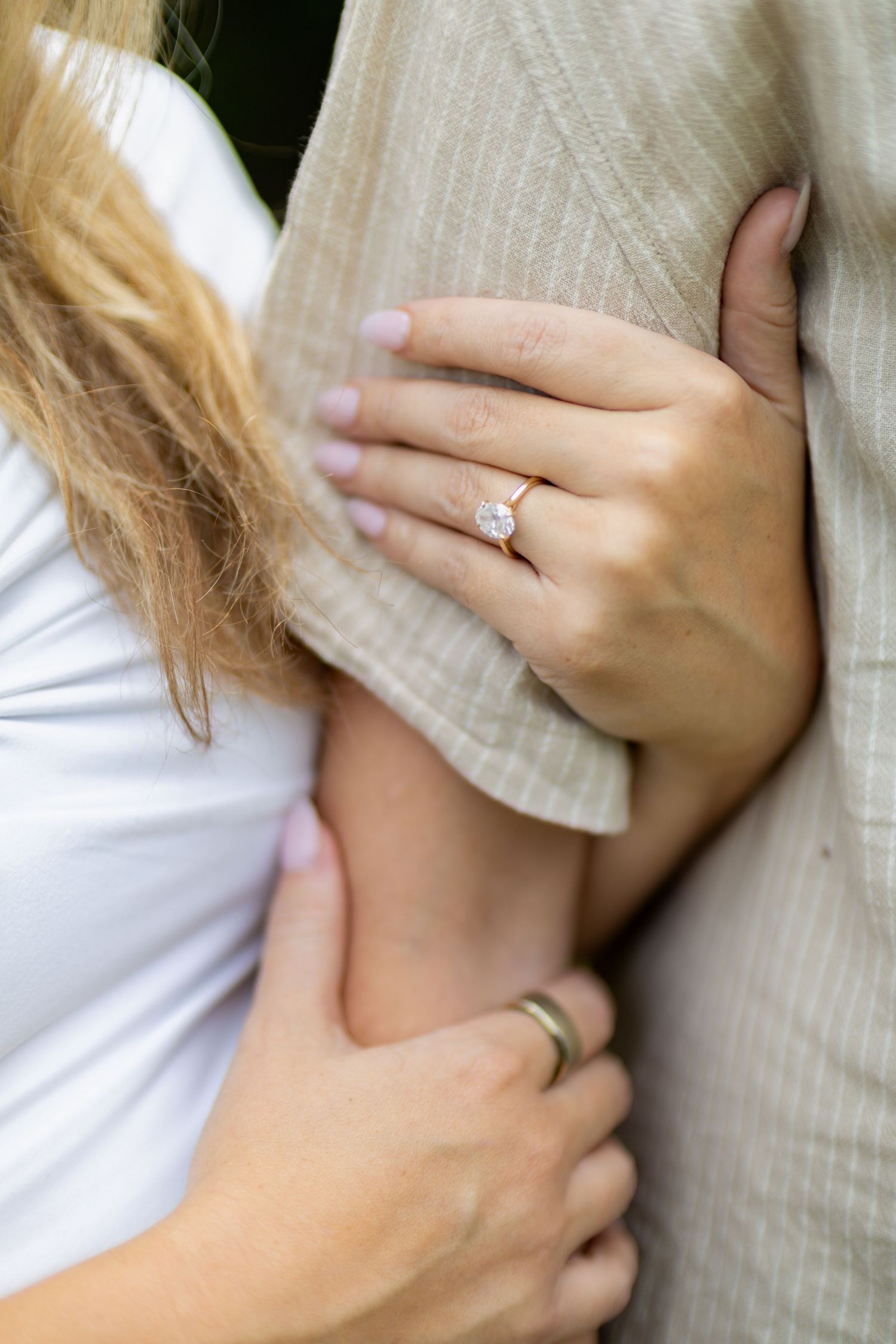 Close-up of a woman's hand with a diamond engagement ring resting on a man's arm as he holds her waist.