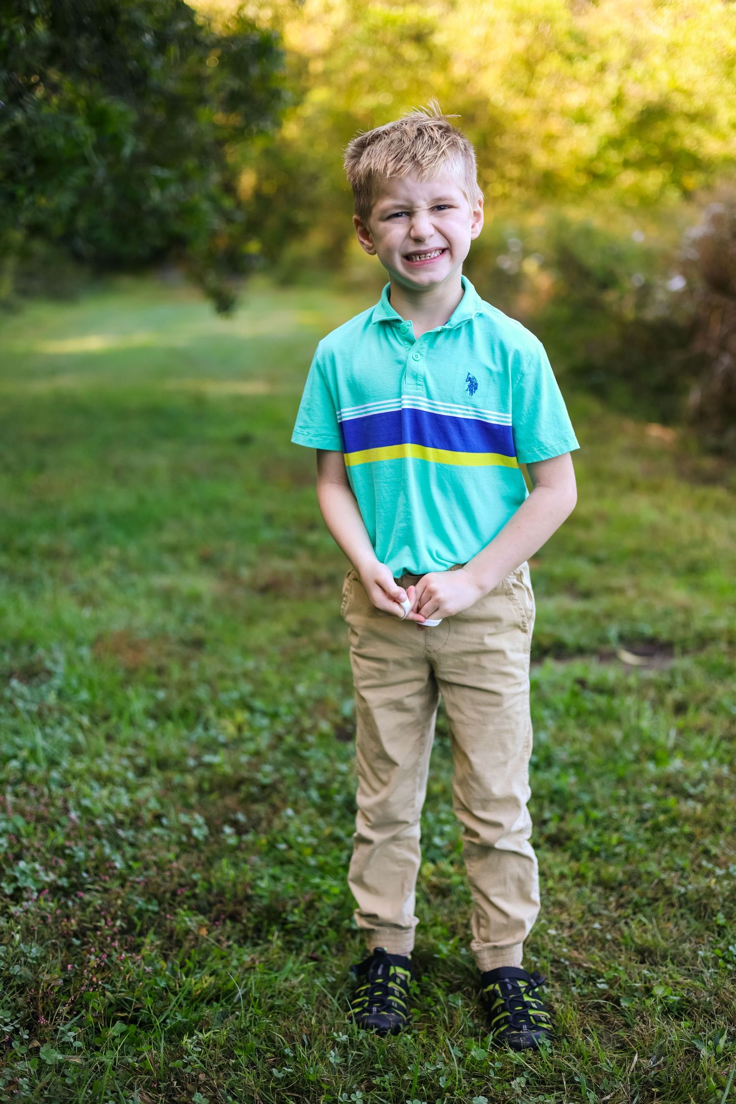 Young child wearing turquoise polo shirt and khaki pants playing outdoors in a grassy area.