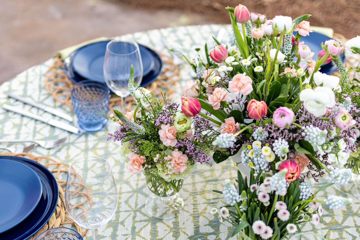 Pink and white floral centerpieces with tulips and roses decorate elegant place settings at a wedding reception.