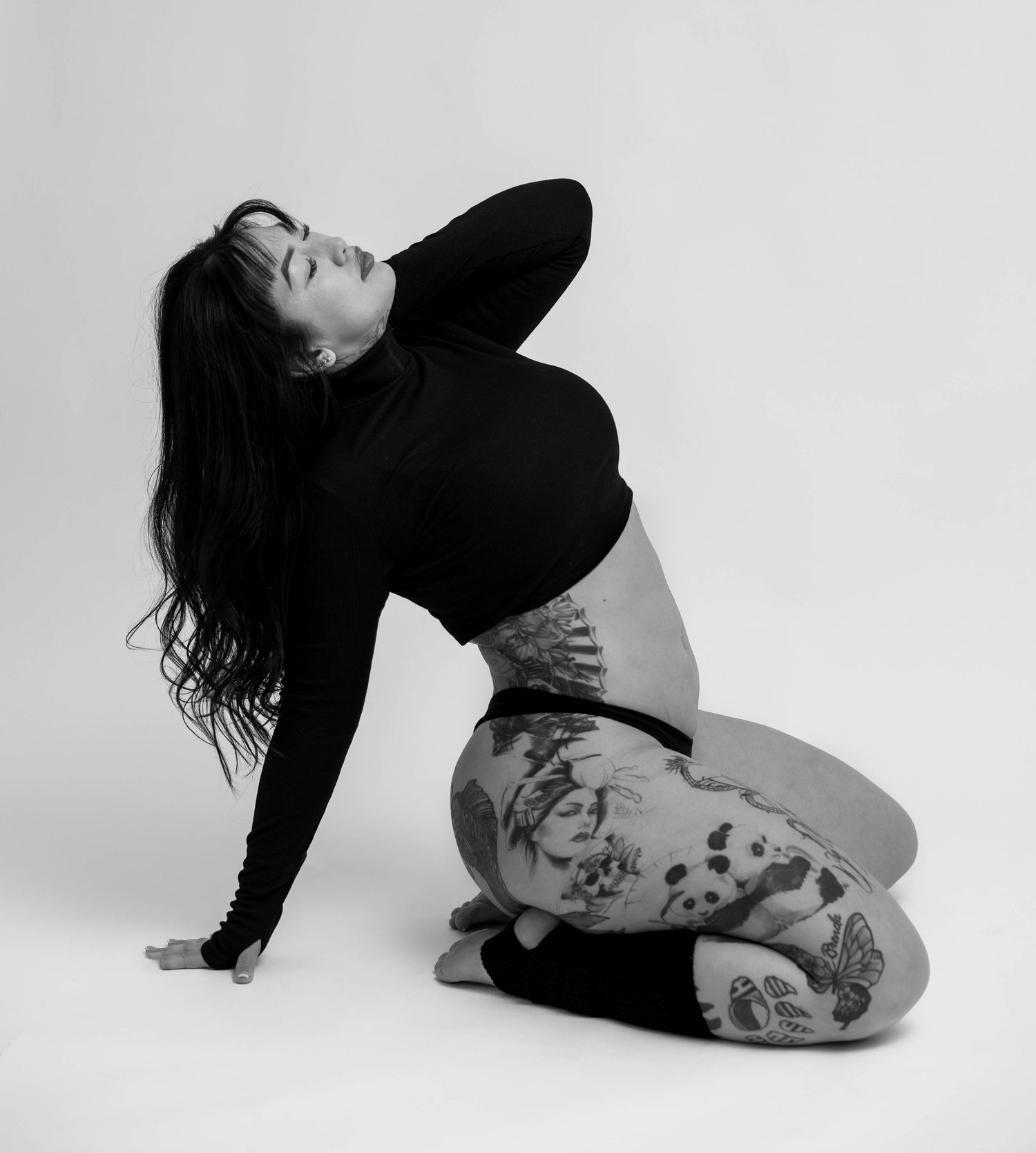 Artistic black and white portrait of a dancer in a black top and patterned leggings posing against white background.