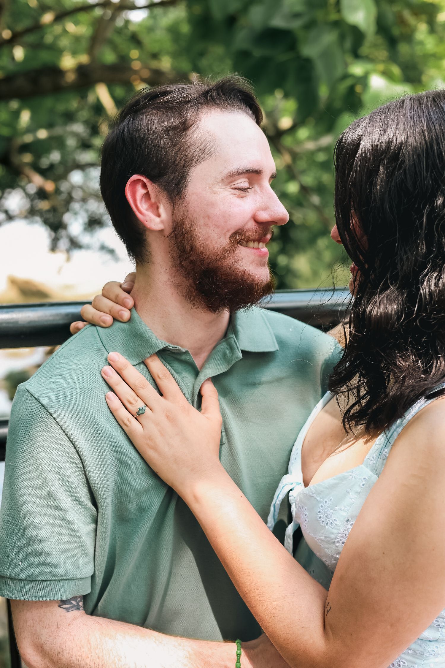 A romantic outdoor moment between a couple as they embrace, with sunlit greenery in the background.