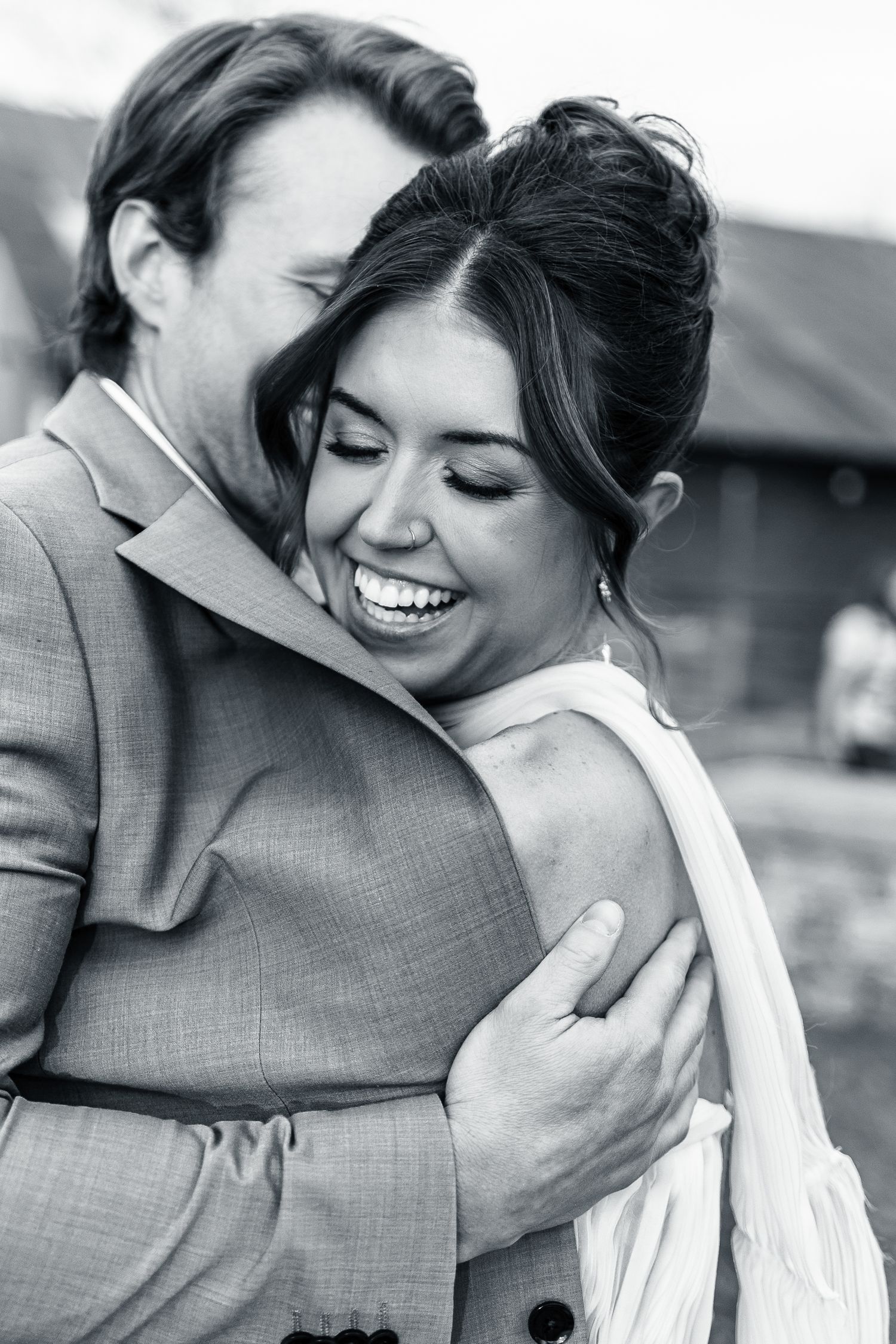 Black and white candid wedding photo capturing a joyful intimate moment between newlyweds embracing and laughing.