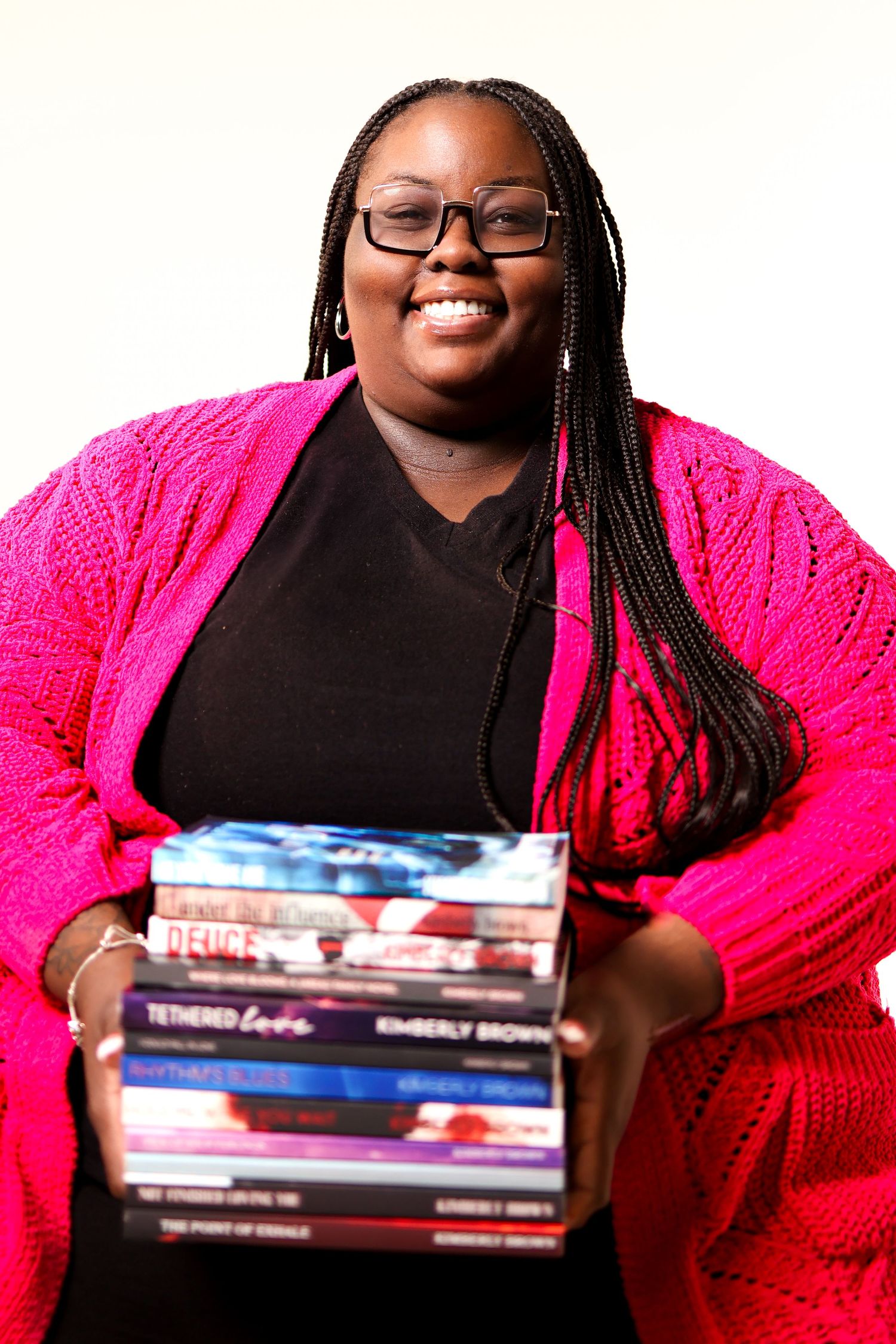 Person in black top and bright pink cardigan smiles while holding stack of books.