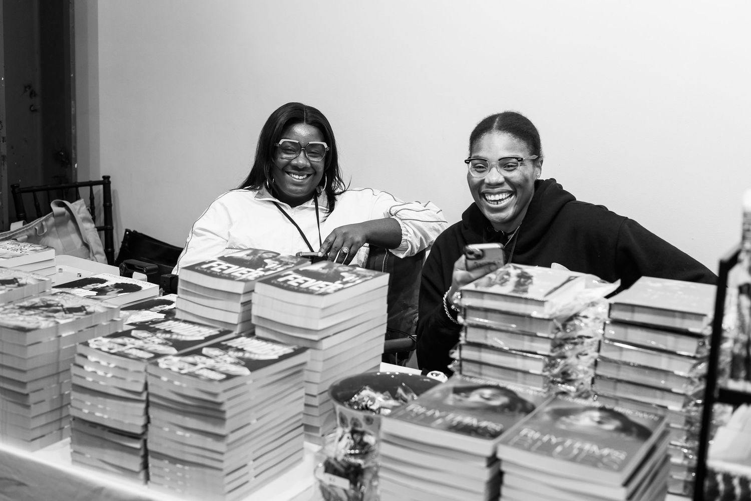 Students sit at a desk with large stacks of textbooks and study materials spread out in front of them.